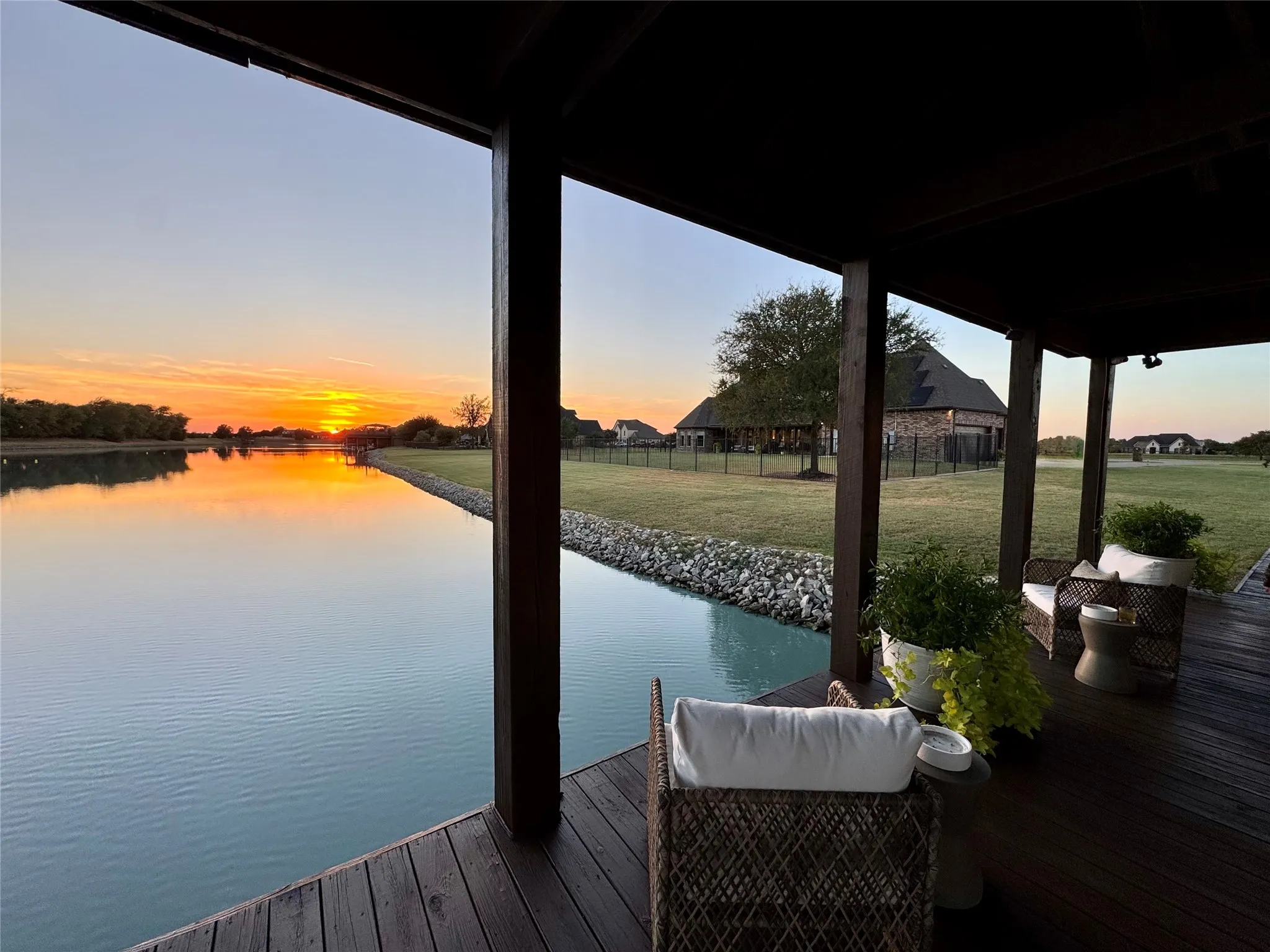 Covered outdoor patio with a dark wood-finish deck, overlooking a serene body of water, and a landscaped lawn