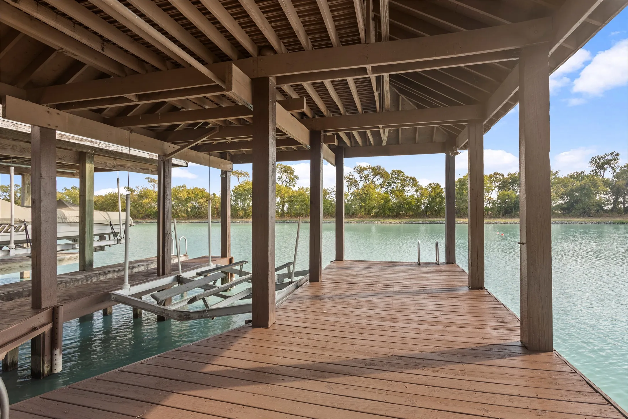 Covered boat dock featuring durable wood decking, exposed wood rafters, and a built-in boat lift
