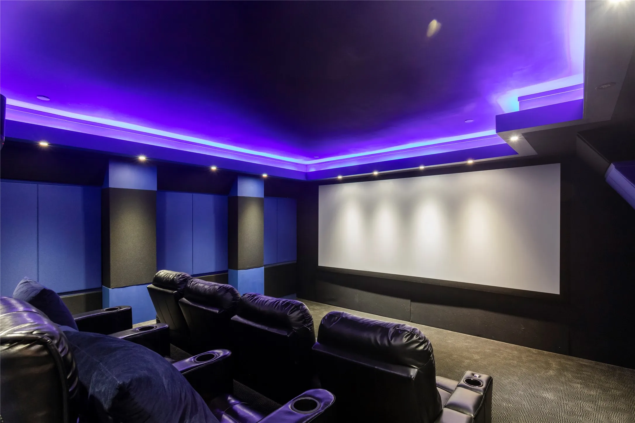 Custom home theater with recessed lighting, ambient cove lighting, large projection screen, and sound-absorbing wall panels