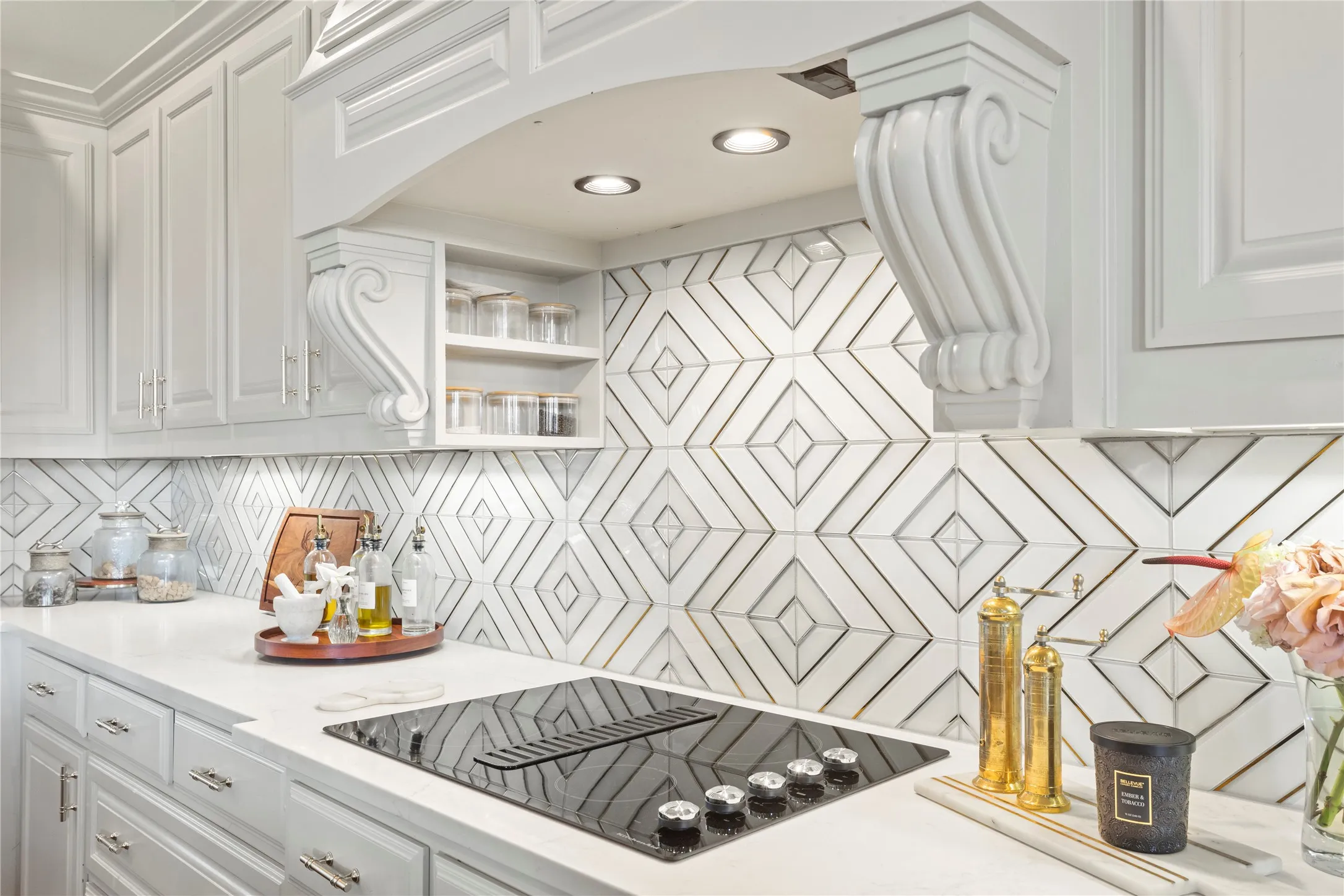 White cabinetry with chrome hardware, an integrated cooktop with downdraft ventilation, geometric pattern backsplash, recessed lighting, and solid surface countertops