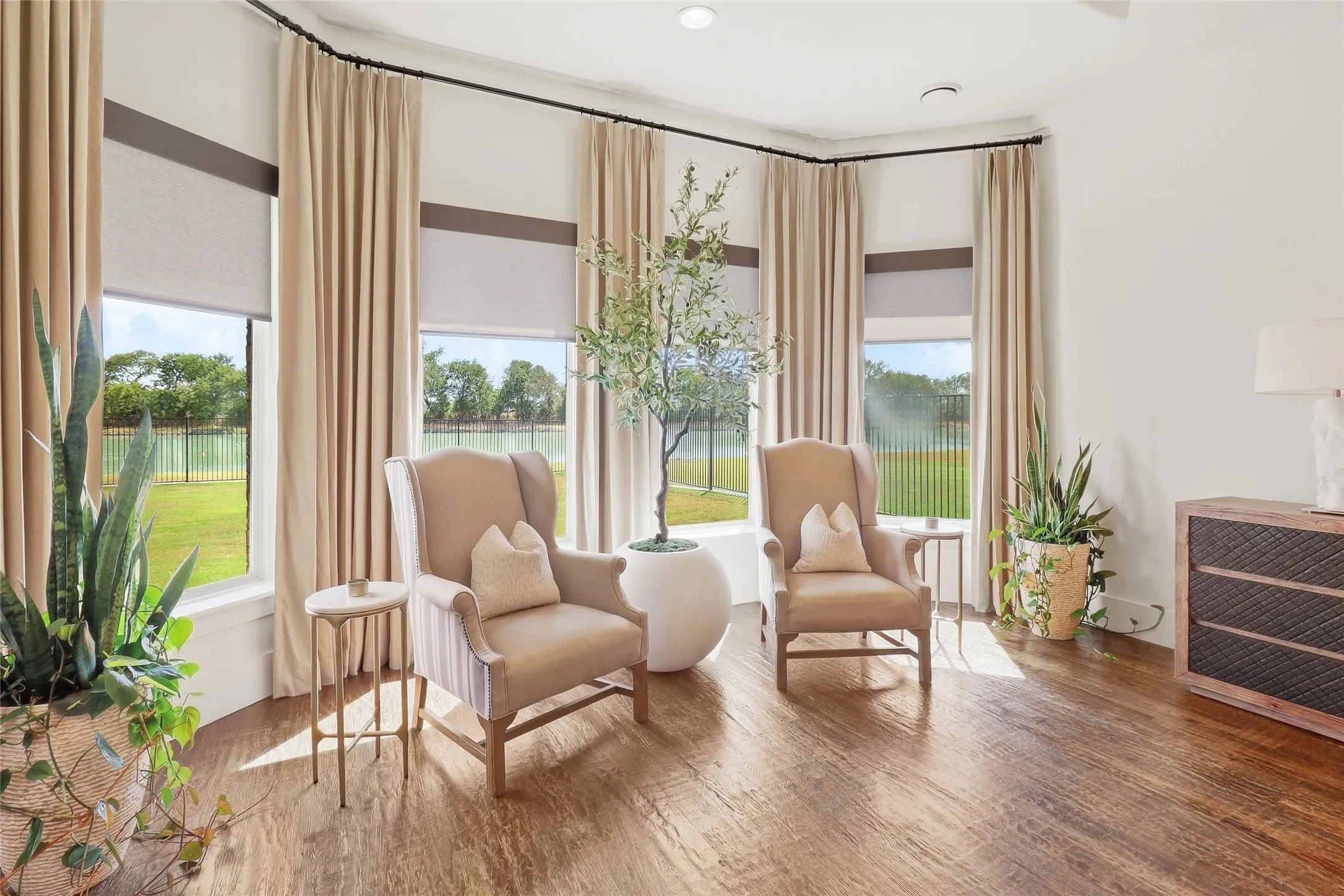 Bay window with roller shades, hardwood-finish flooring, and light-toned curtains