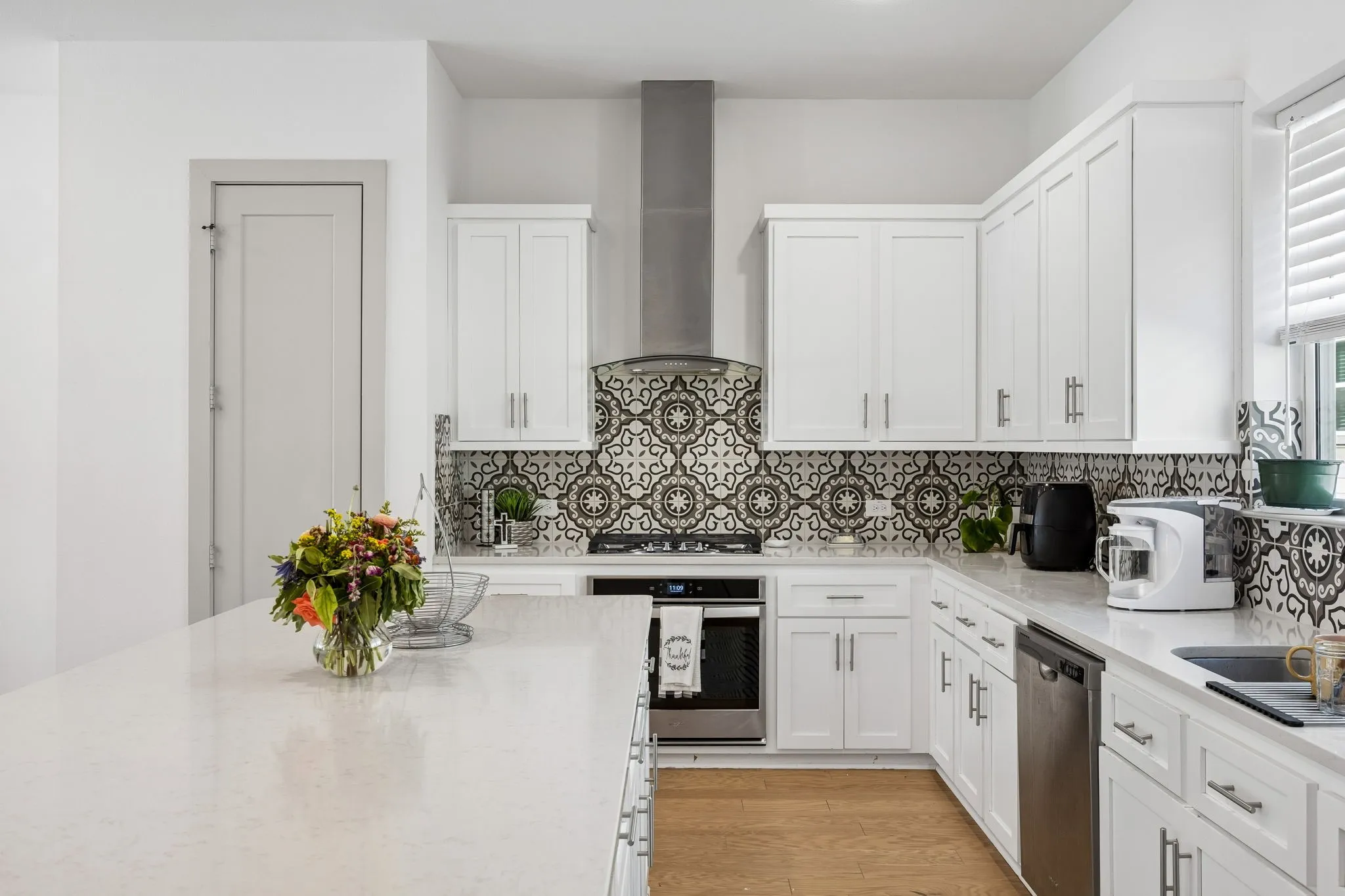 The kitchen is a dream with a large quartz island, a stainless gas range, stainless vent hood and designer tile backsplash.