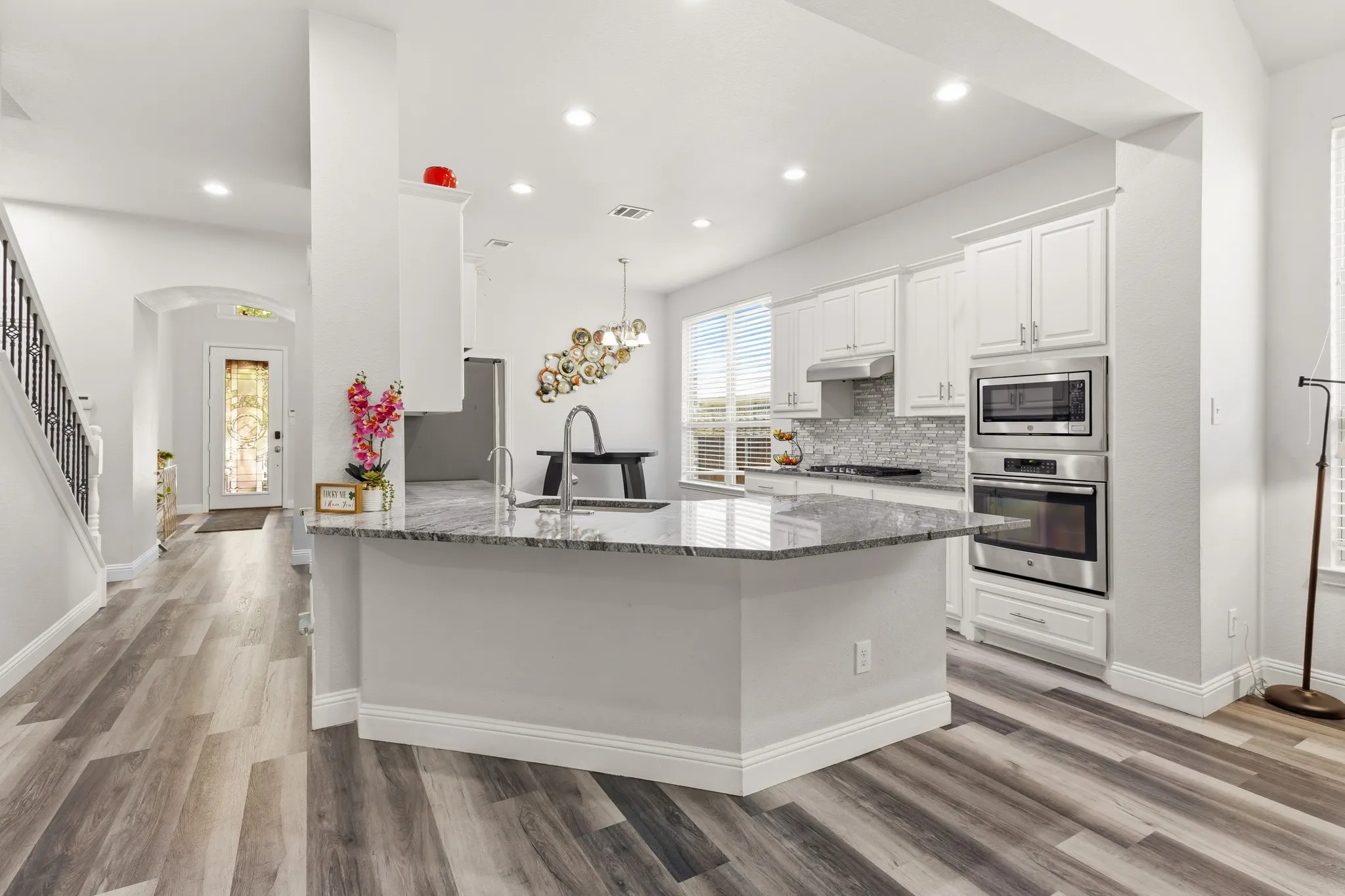 Modern kitchen island with granite countertop, white cabinetry, stainless steel appliances, and wood-finish flooring