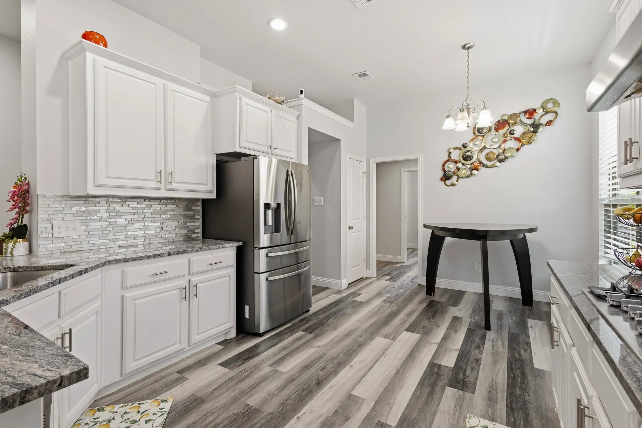 White cabinetry, stainless steel refrigerator, granite countertops, tile backsplash, and wood-finish flooring