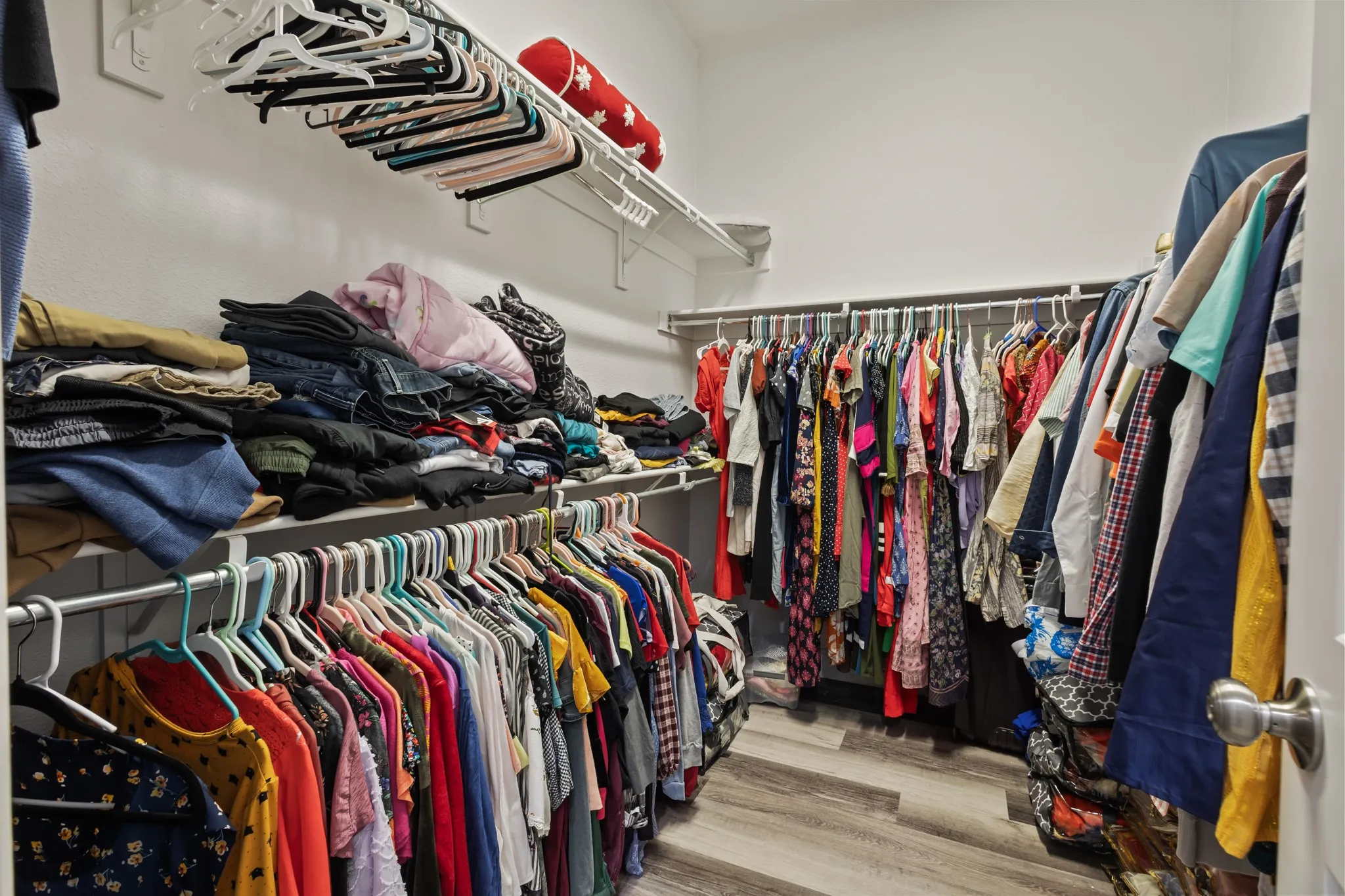 Walk-in closet featuring tiered shelving, multiple clothing rods, and wood-finish flooring