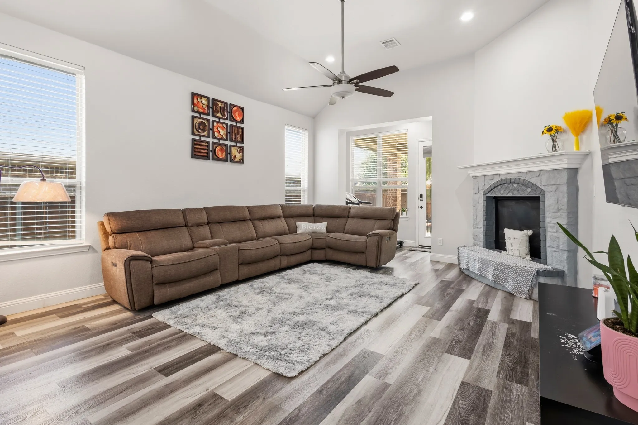 Vaulted ceilings, wood-finish flooring, recessed lighting, ceiling fan, and a stone-surround fireplace with mantel