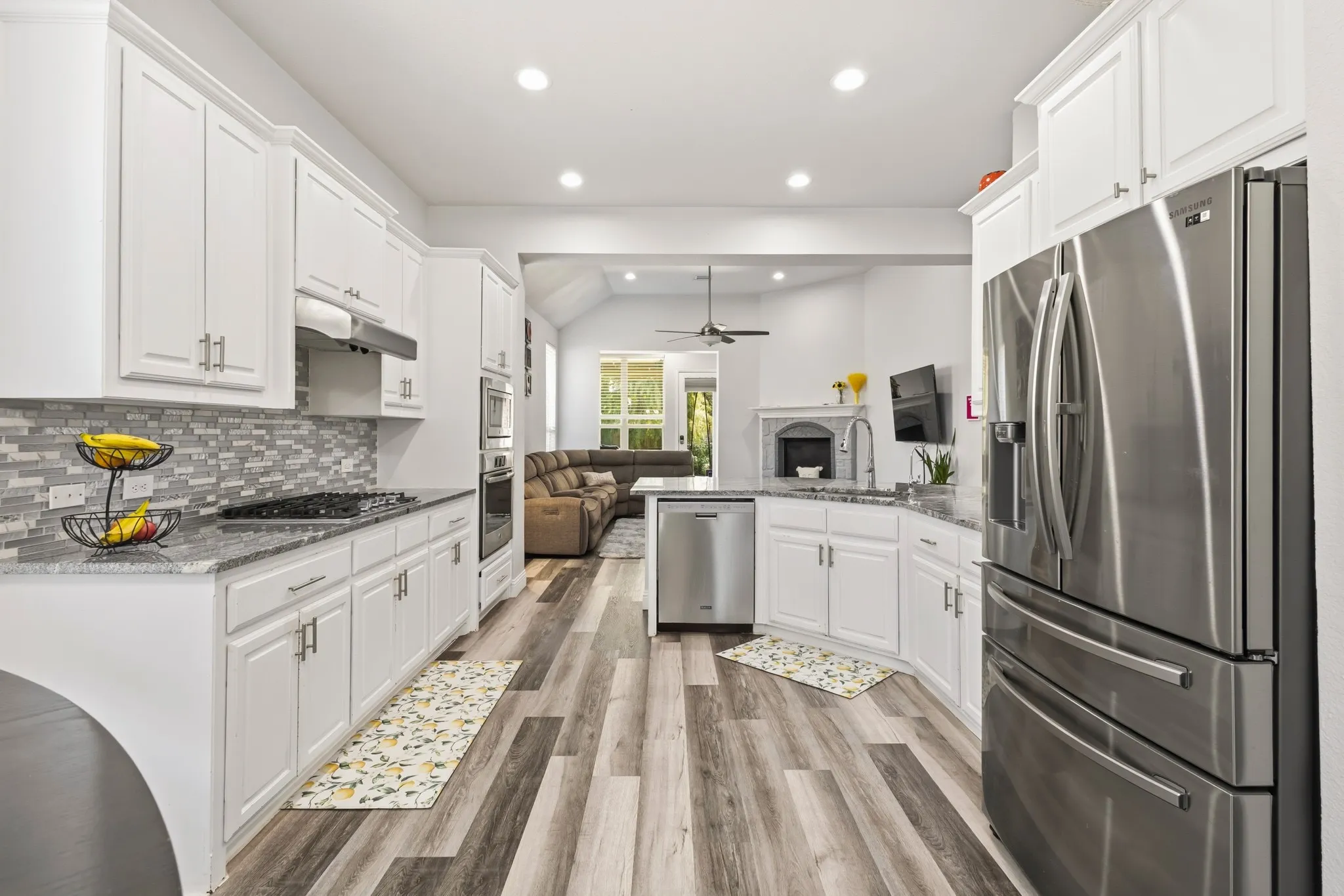 Gourmet kitchen featuring white cabinetry, stainless steel appliances, granite countertops, a mosaic tile backsplash, and wood-finish flooring