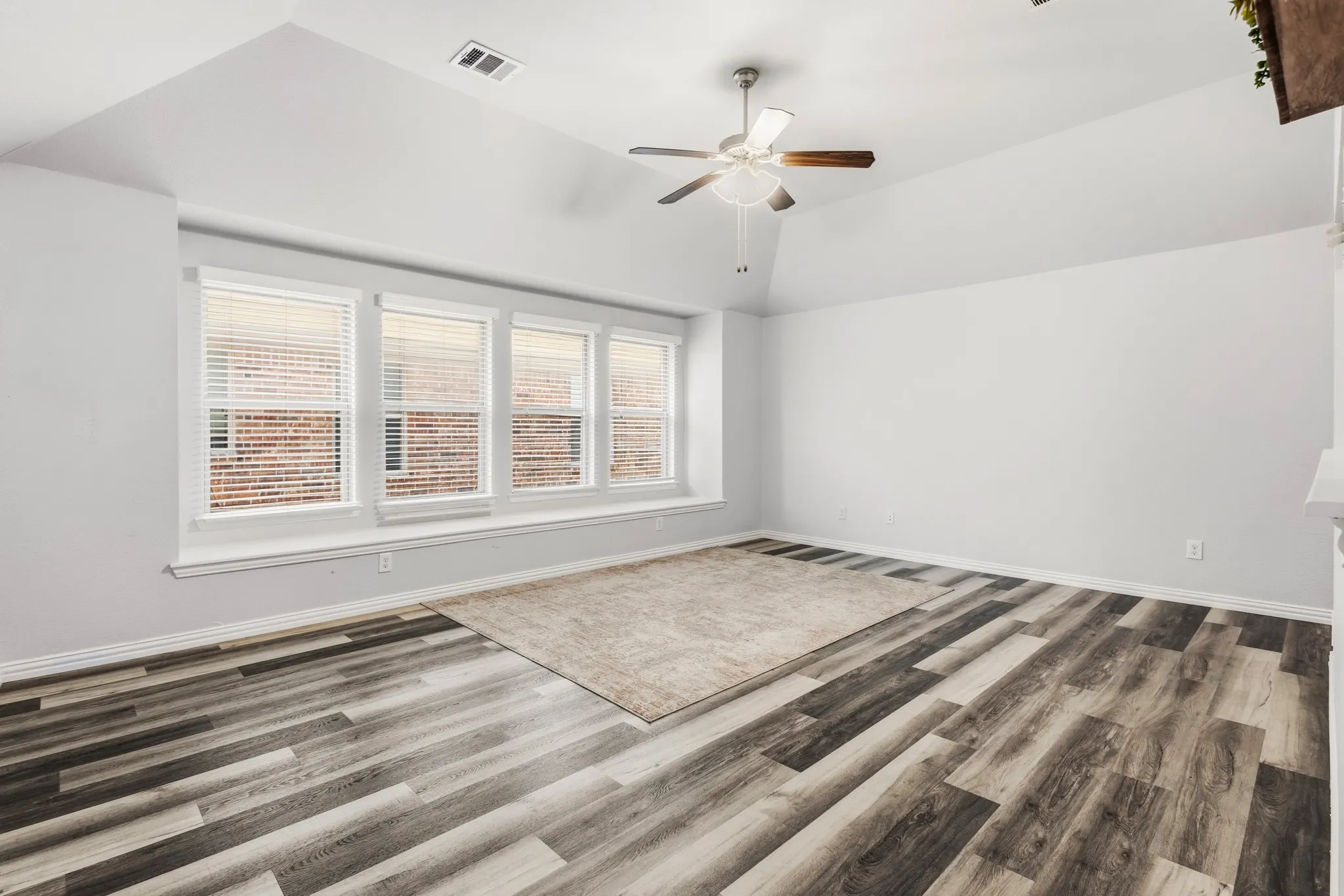 Vaulted ceiling with a ceiling fan, wood-finish flooring, and multiple windows with blinds
