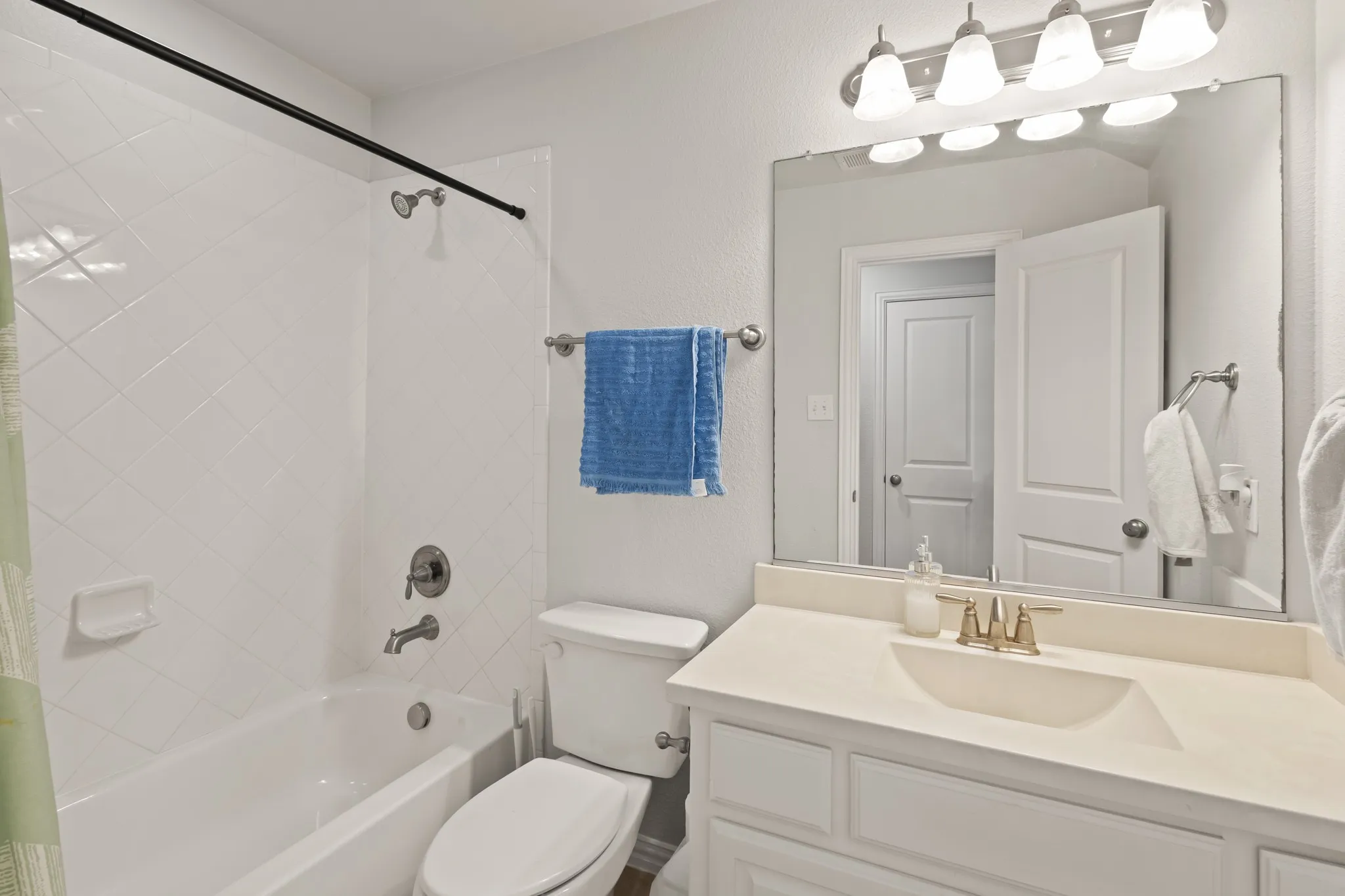 Bathroom featuring a white bathtub with tile surround, a built-in vanity with an integrated sink, a large wall-mounted mirror, and a multi-bulb vanity light fixture