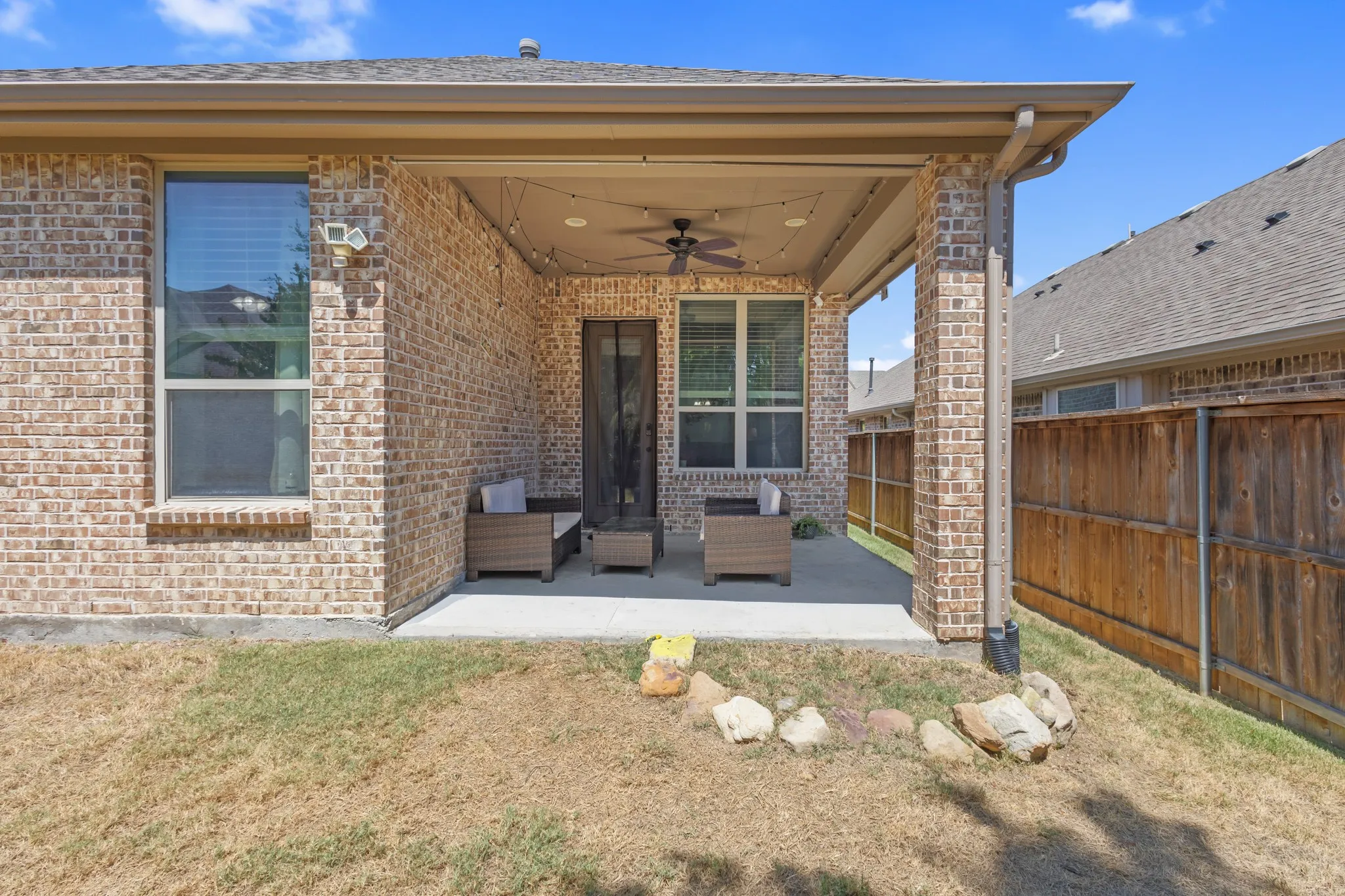 Covered patio featuring a ceiling fan, string lighting, and brick columns