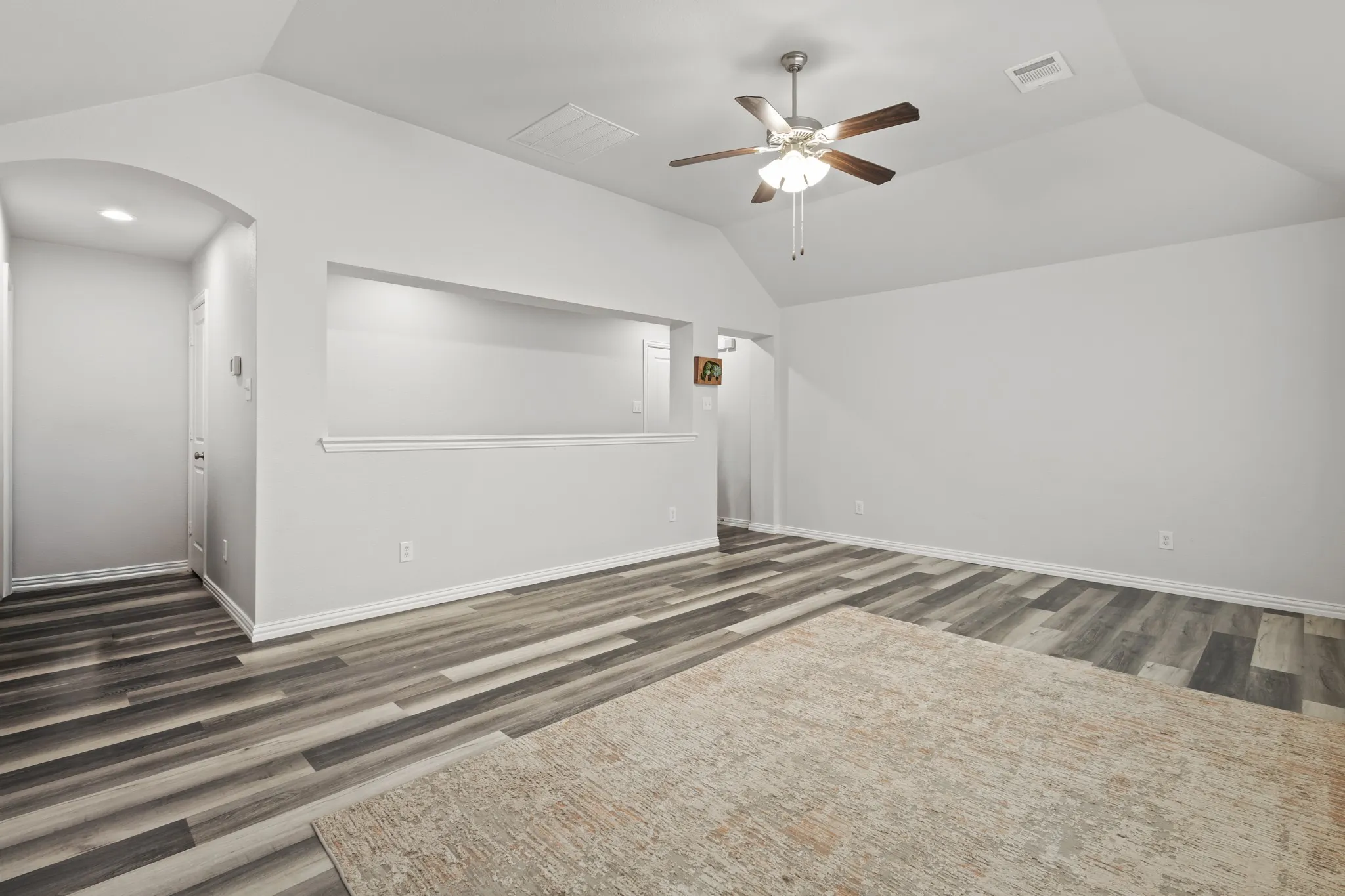 Vaulted ceiling with a ceiling fan, wood-finish flooring, recessed lighting, and an arched hallway entry