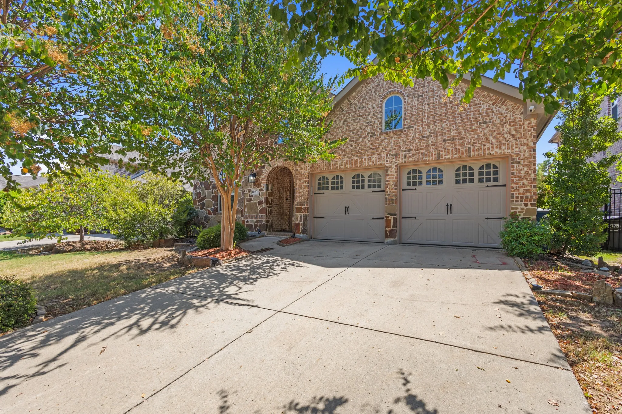 Brick and stone exterior with an arched entry, two-car garage with decorative doors, arched window, and mature landscaping