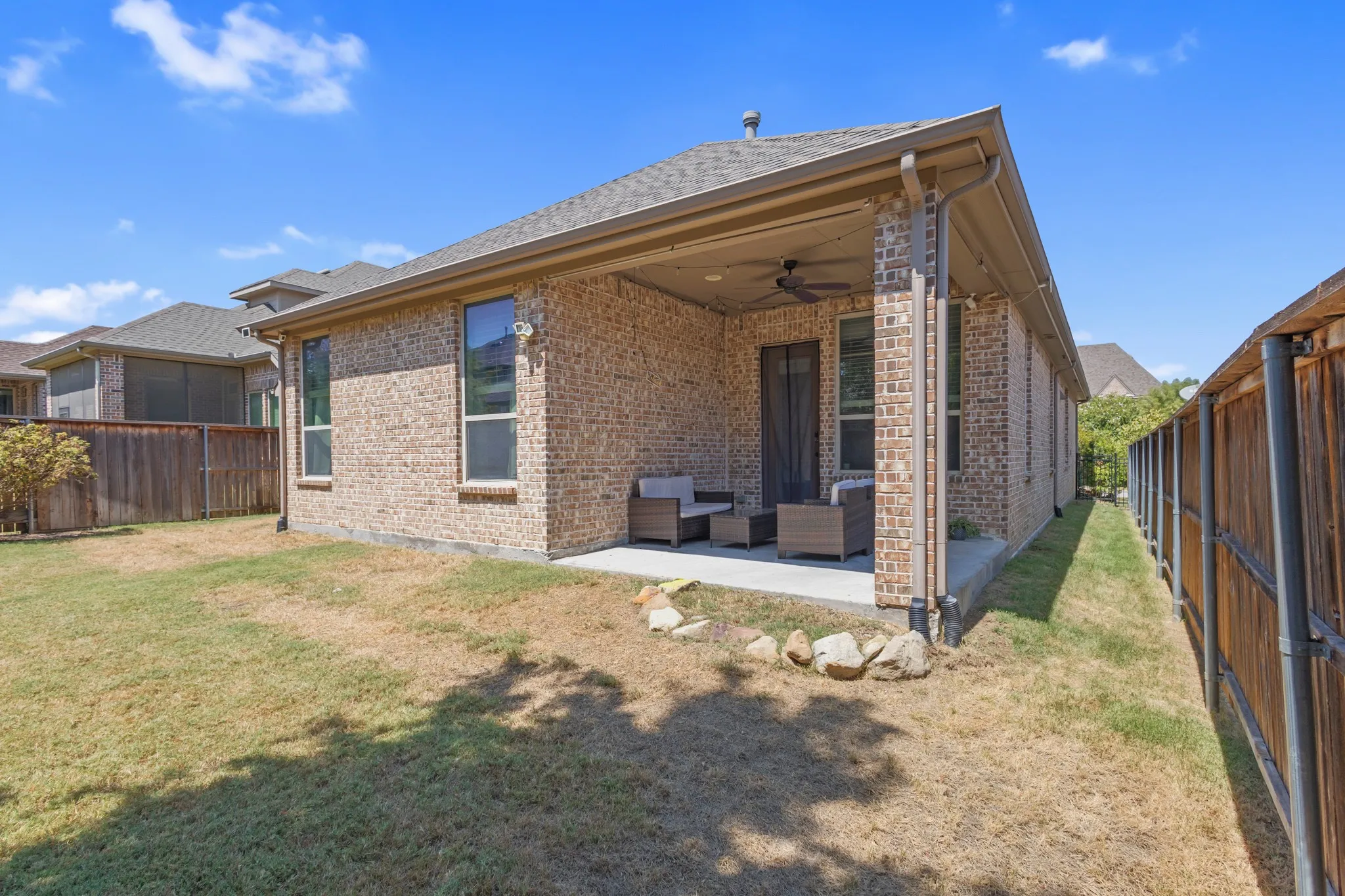 Brick exterior with a covered patio, ceiling fan, and fenced yard
