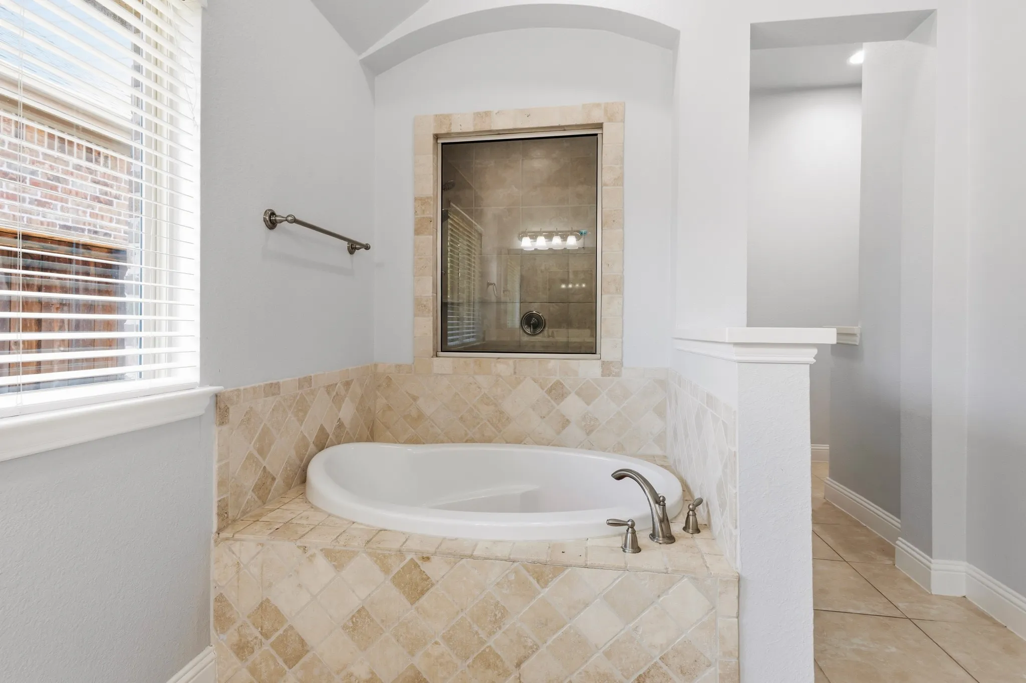 Recessed soaking tub with neutral-toned tile surround, brushed nickel fixtures, and arched alcove