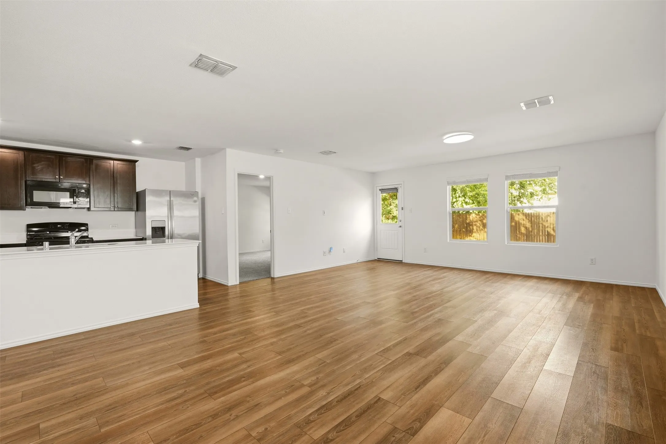 Expansive open-concept living area with wood-finish flooring, two large windows, a white entry door, and recessed lighting