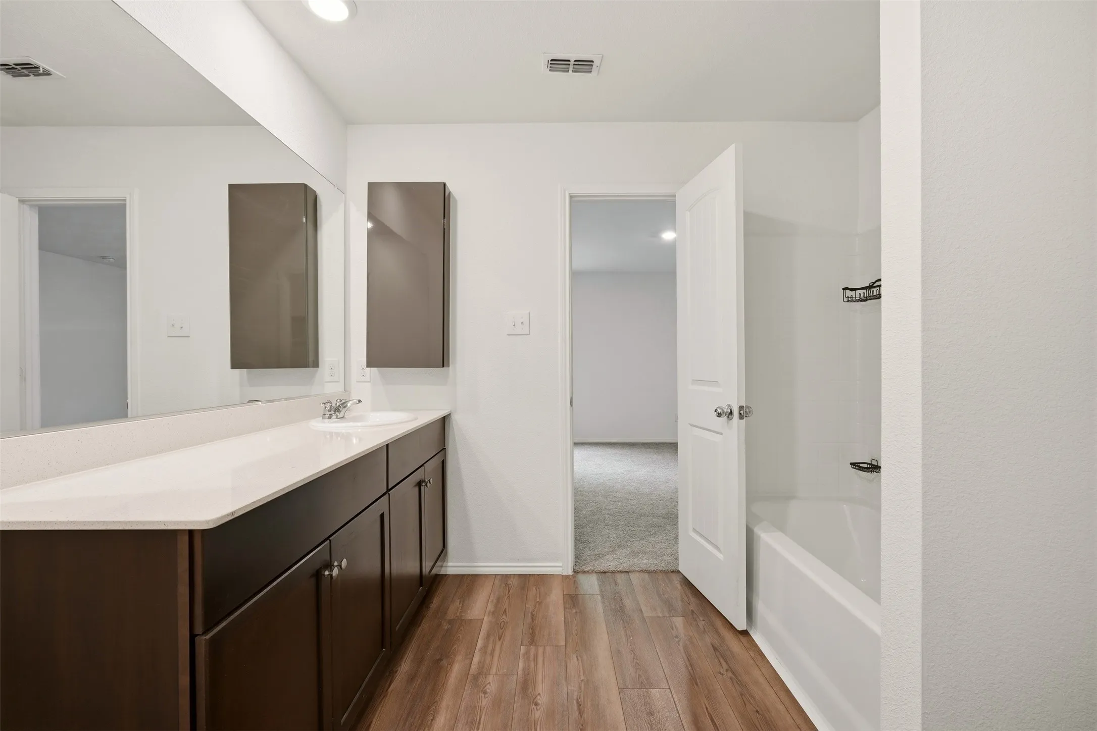Vanity with integrated sink, wood-finish flooring, built-in wall cabinets, and a white bathtub