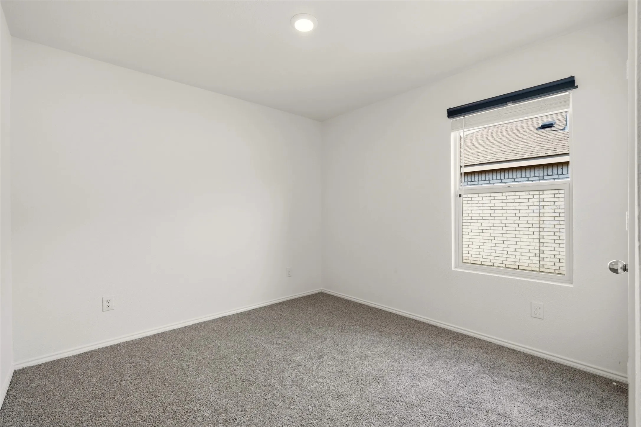 Neutral-toned carpeting and walls, recessed ceiling lighting, and a single window with blinds and a roller shade