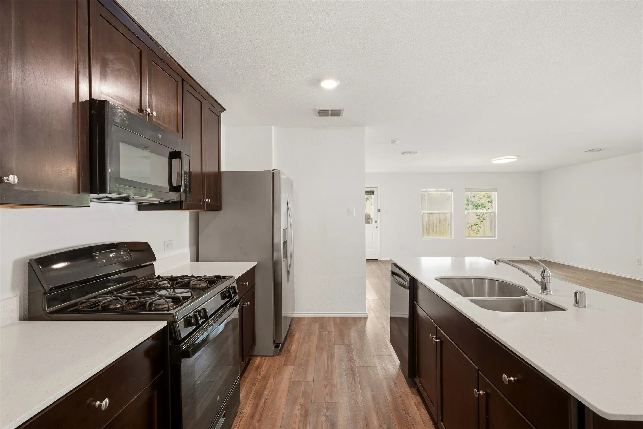 Kitchen featuring dark wood cabinetry, white countertops, stainless steel appliances, and wood-finish flooring