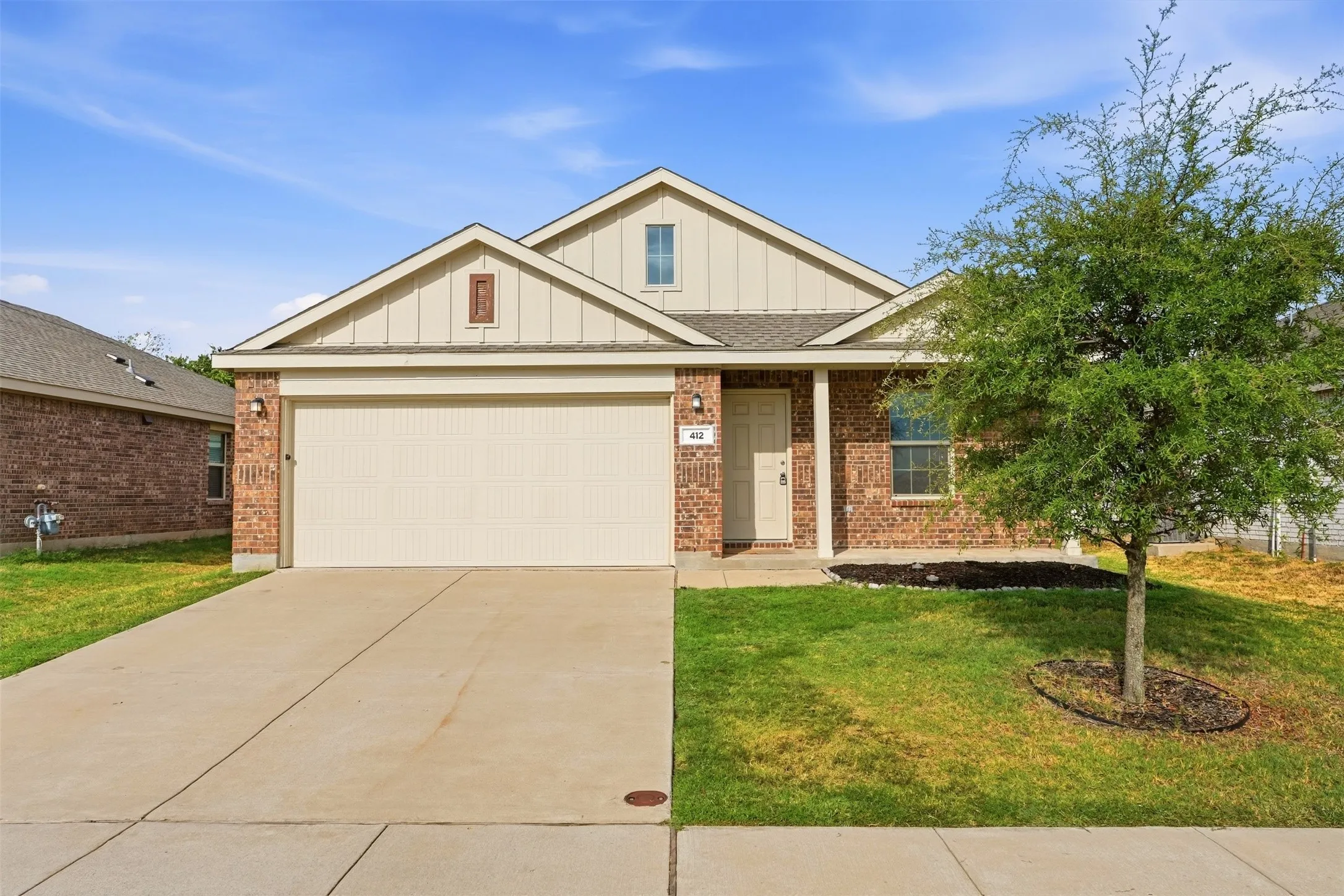 Brick and siding exterior with an attached garage, covered entry, front lawn, and concrete driveway