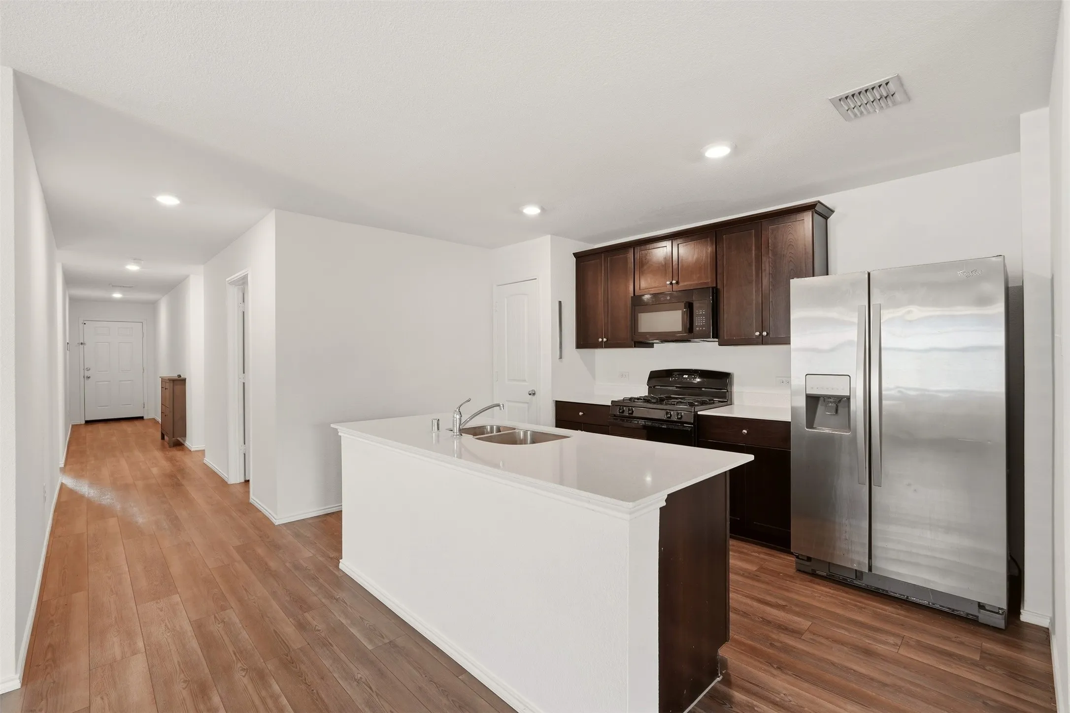 Kitchen featuring wood-finish flooring, dark wood cabinetry, a center island with sink, stainless steel appliances, and recessed lighting