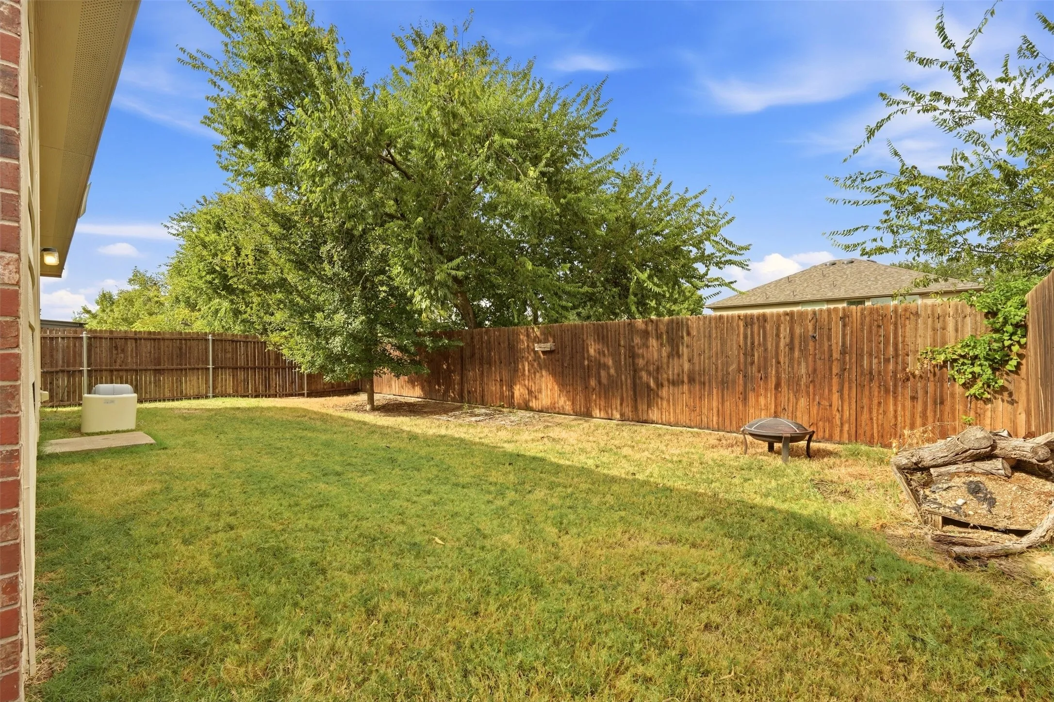 Expansive backyard featuring a wood fence, mature trees, and a brick exterior wall