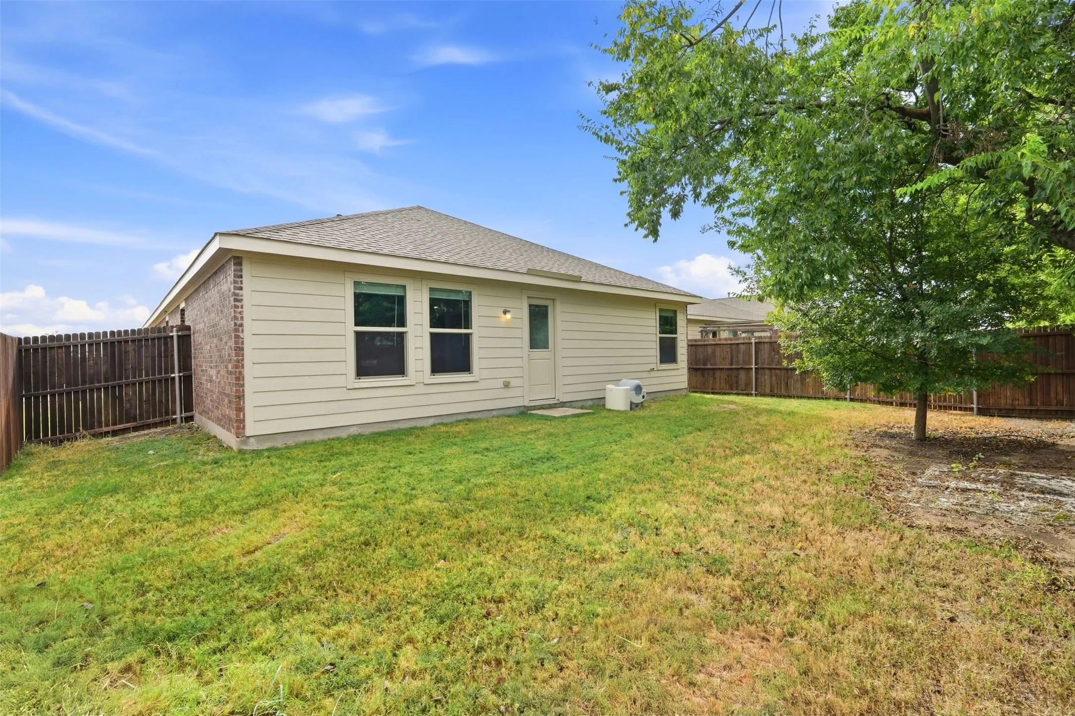Private backyard with wood privacy fencing, brick and siding exterior, and mature tree
