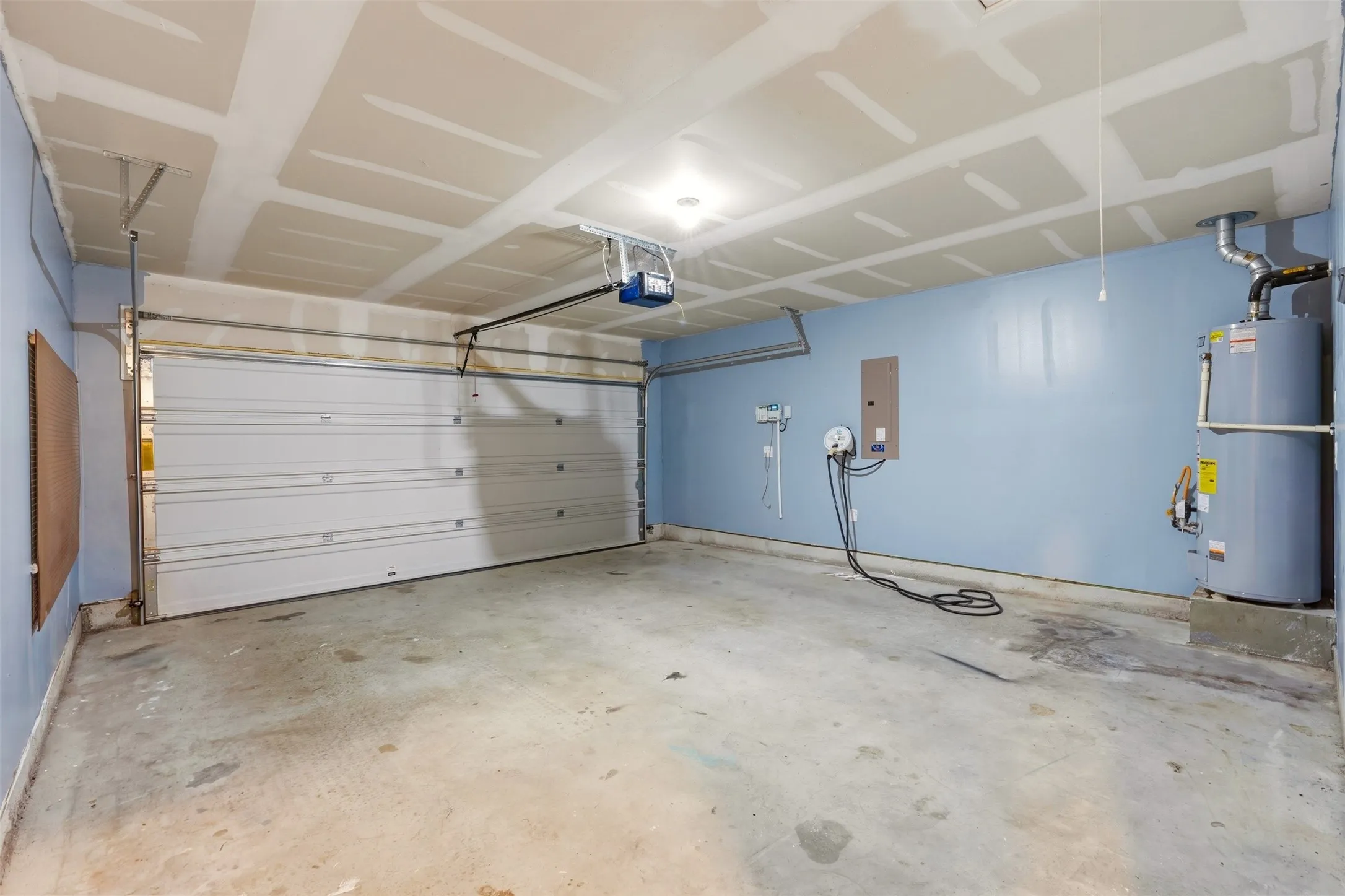 Garage with a concrete floor, a white sectional garage door, a ceiling-mounted garage door opener, and a wall-mounted water heater
