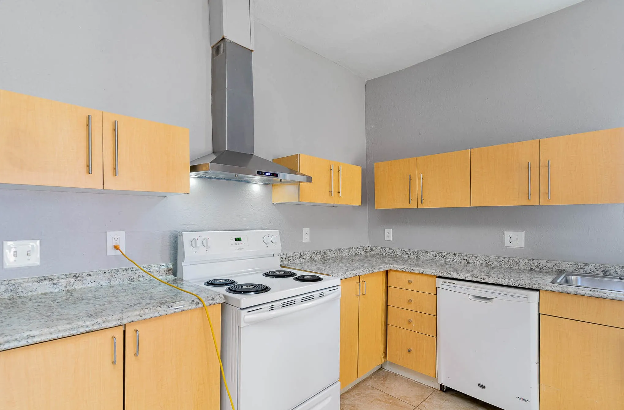 Kitchen featuring white appliances, wall chimney exhaust hood, light tile patterned flooring, a sink, and light brown cabinetry