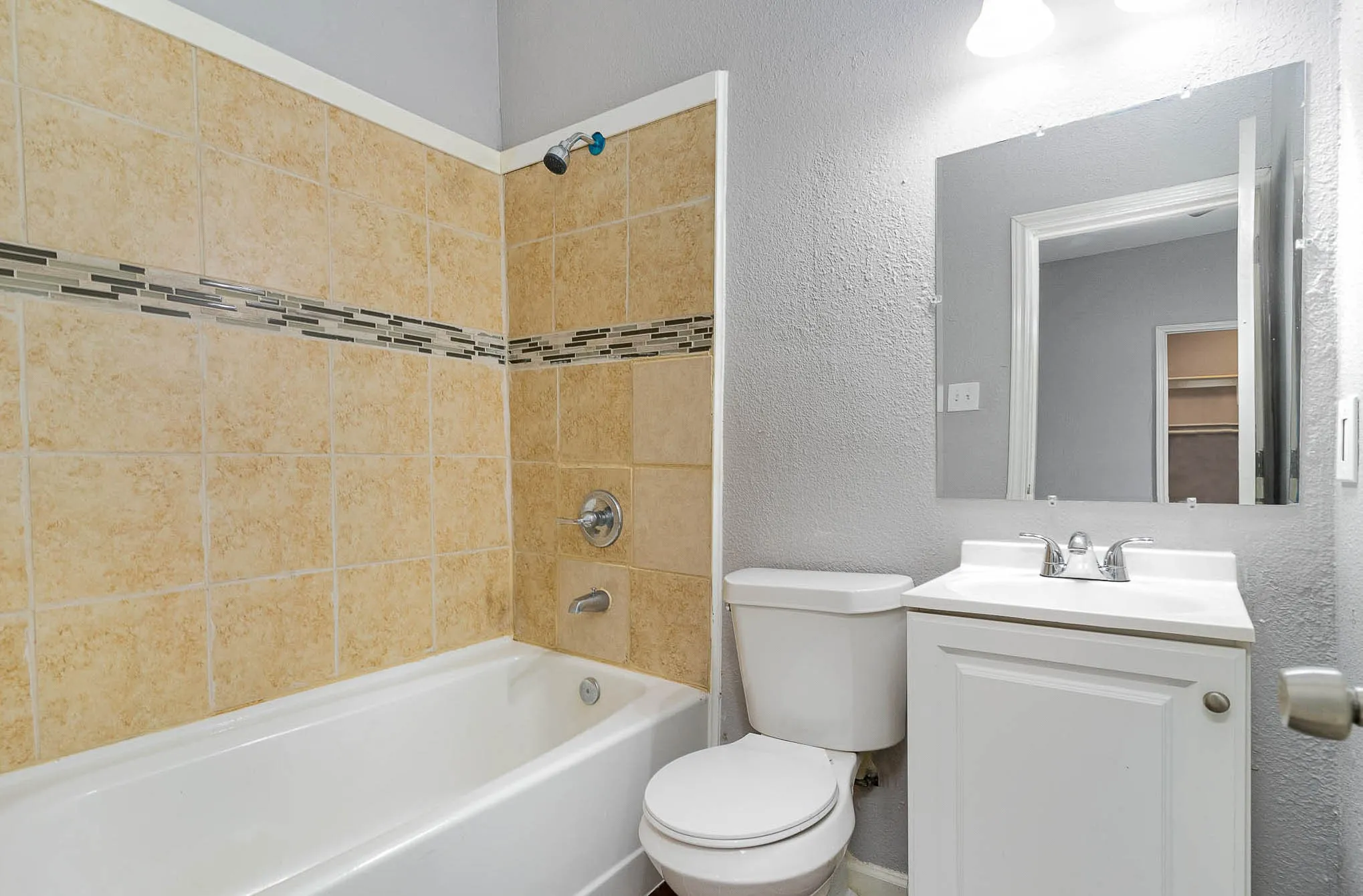 Bathroom featuring a textured wall, toilet, vanity, and shower / washtub combination