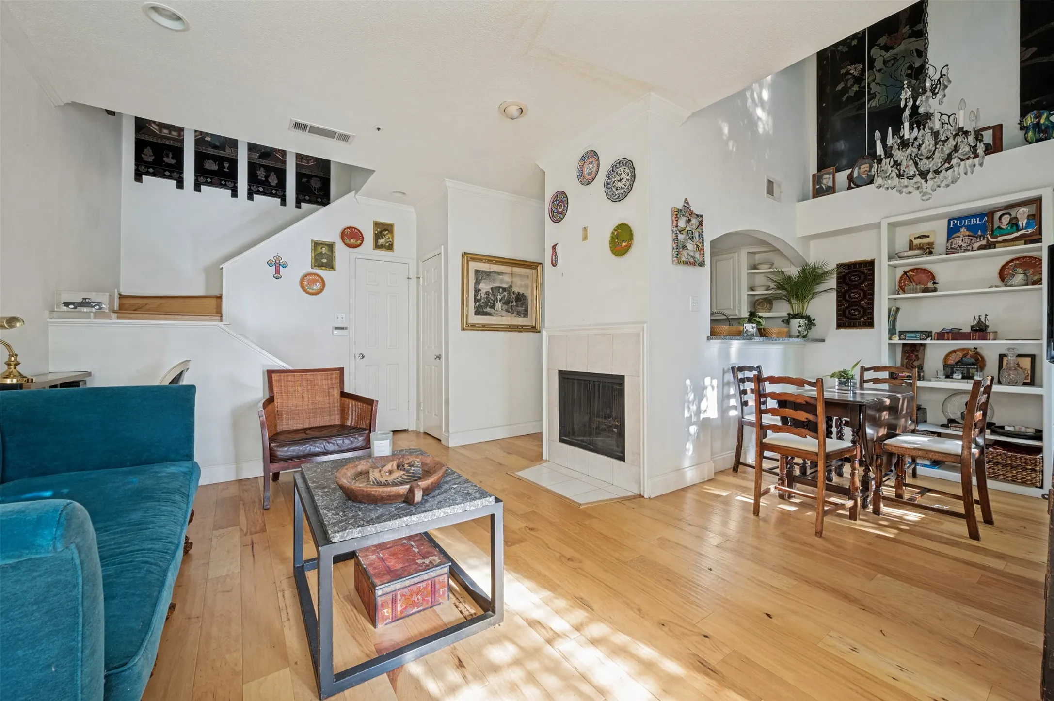 Hardwood flooring throughout, a tiled fireplace with hearth, a built-in shelving unit, a chandelier, and an arched pass-through window