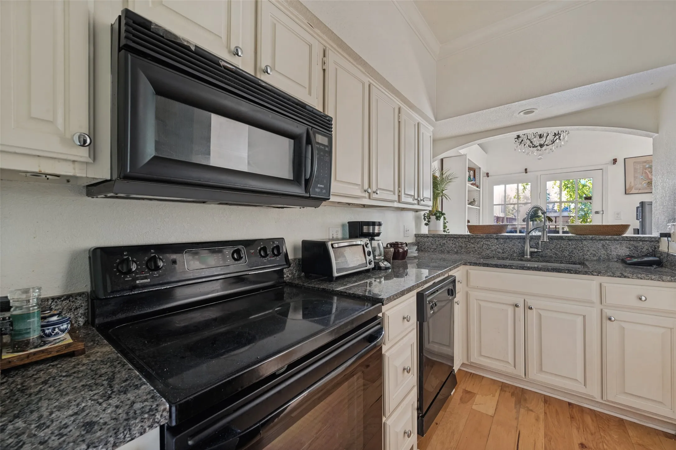 White cabinetry with chrome hardware, dark stone-finish countertops, black built-in microwave, black electric range, and wood-finish flooring