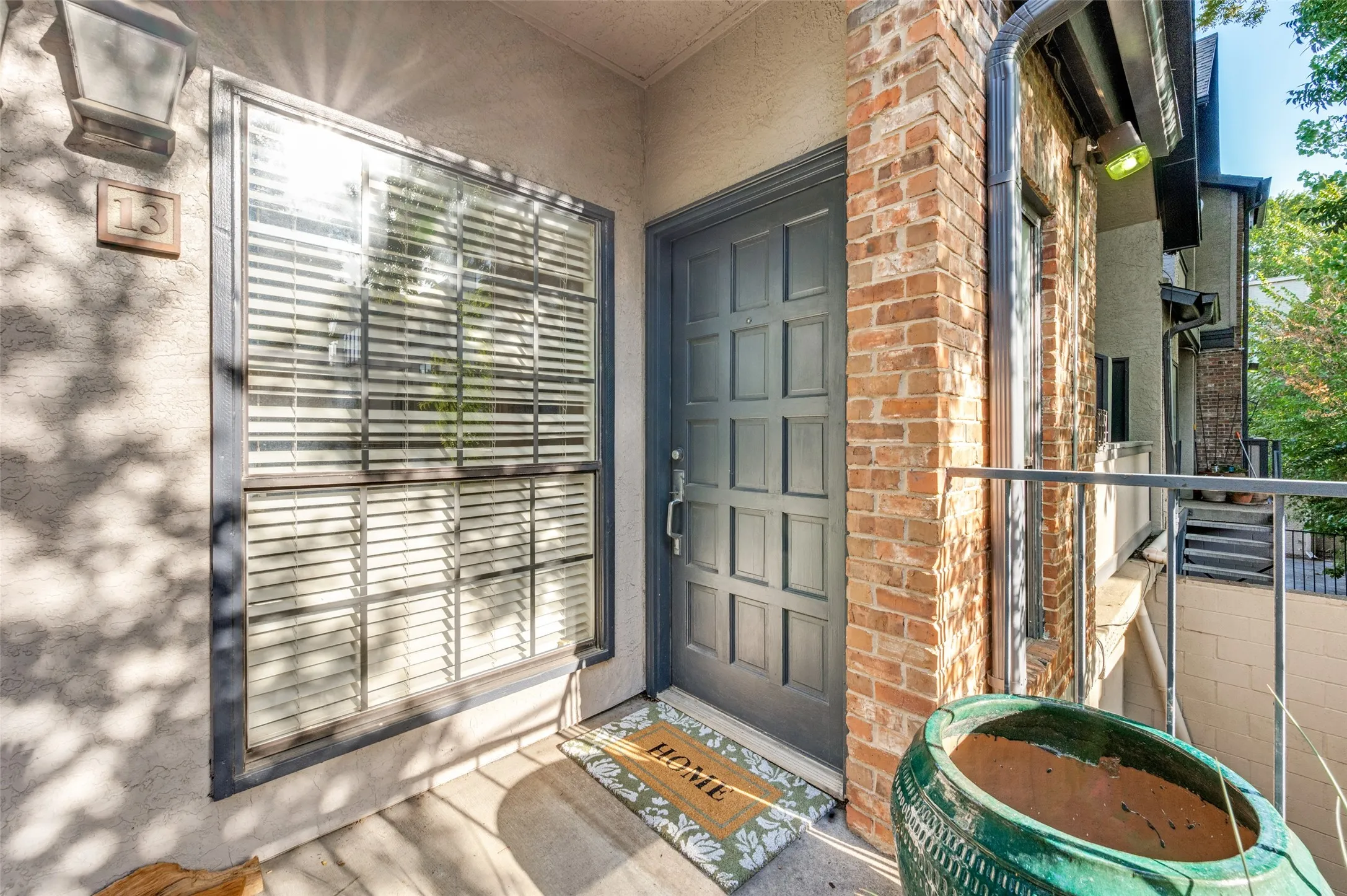 Brick facade with a paneled entry door, a window featuring horizontal blinds, and a metal railing