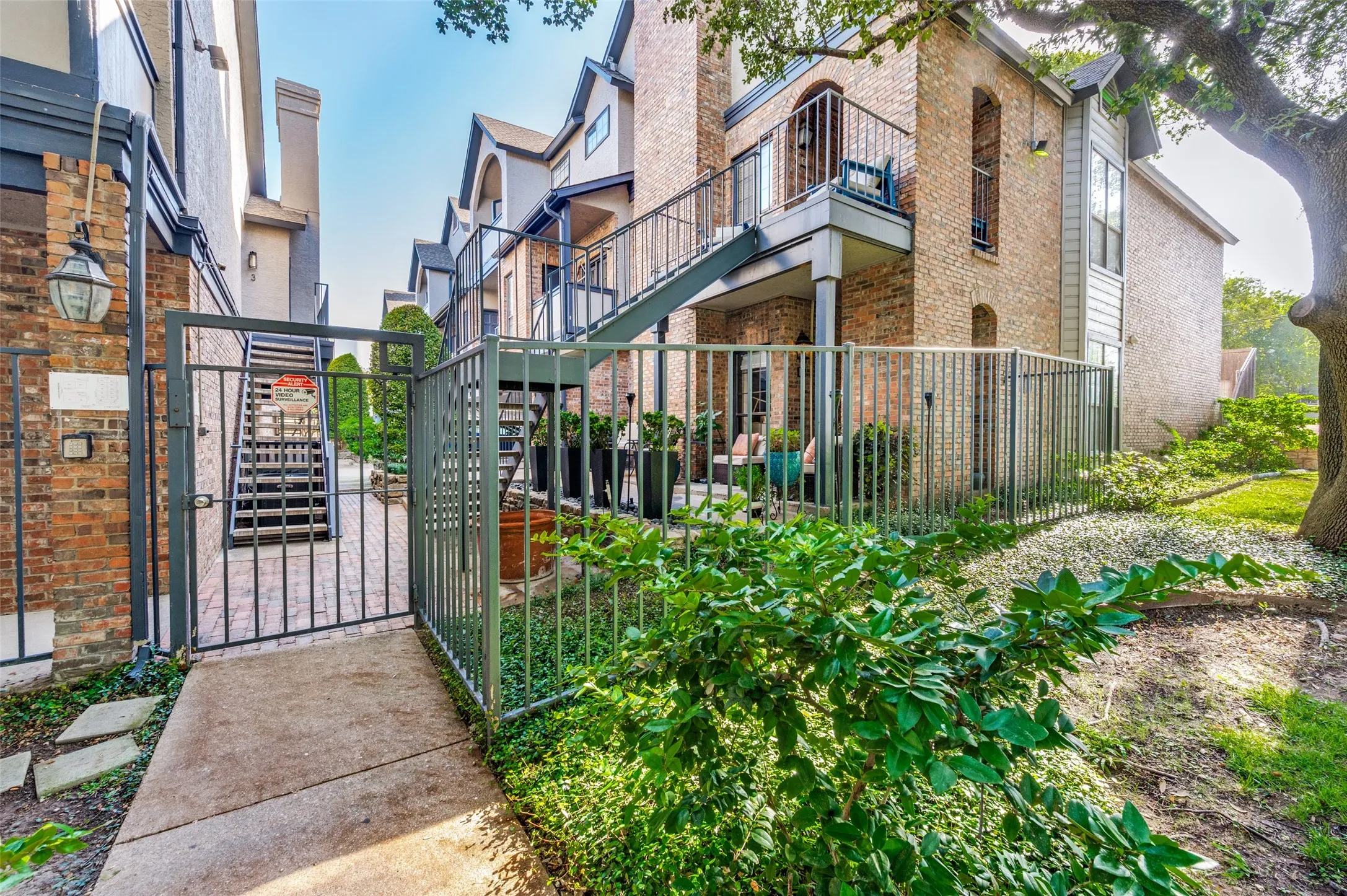 Brick exterior with a private fenced patio, dedicated outdoor staircase, and mature landscaping