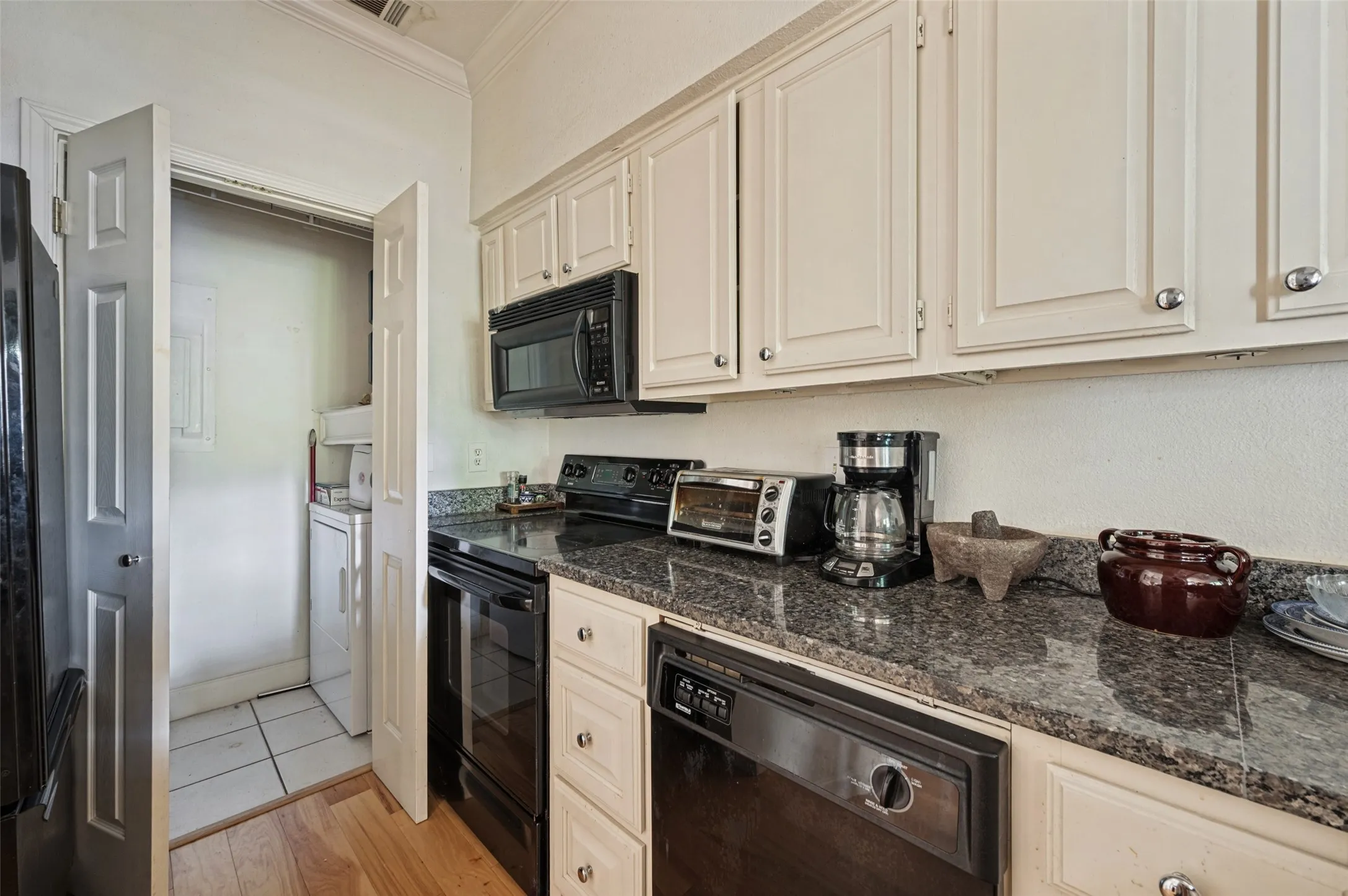 Kitchen featuring upper and lower cabinetry, dark stone countertops, black appliances, and wood-finish flooring