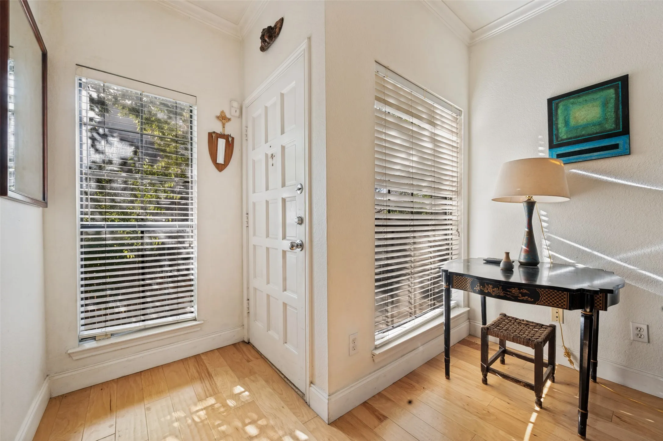 Entryway featuring light wood flooring, a paneled door, and two large windows with blinds
