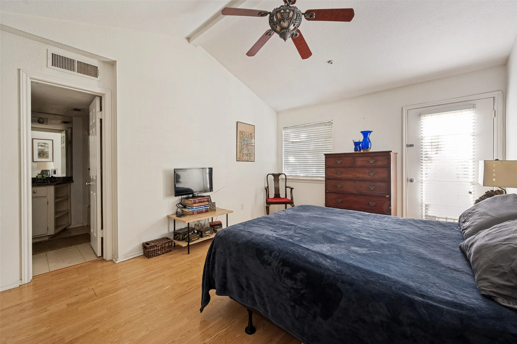Vaulted ceiling with an ornate ceiling fan, wood-finish flooring, and an exterior door