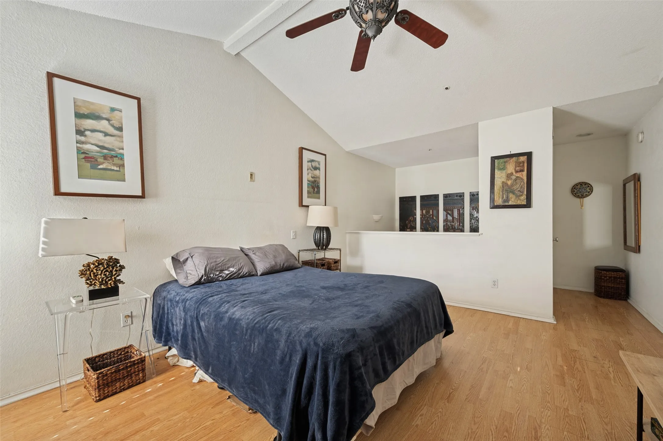 Vaulted ceilings, wood-finish flooring, half-height wall, white painted walls, and ceiling fan with integrated lighting