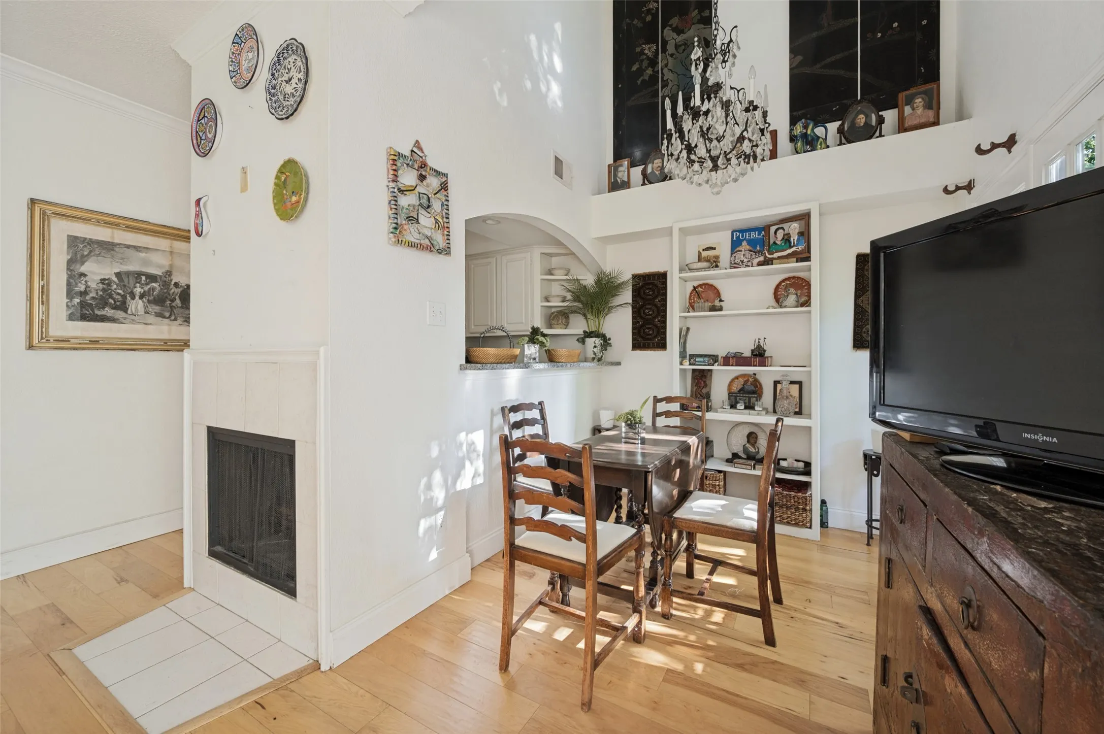 Fireplace with tile surround, wood-finish flooring, built-in shelving, high ceilings, and a kitchen pass-through with an arched opening