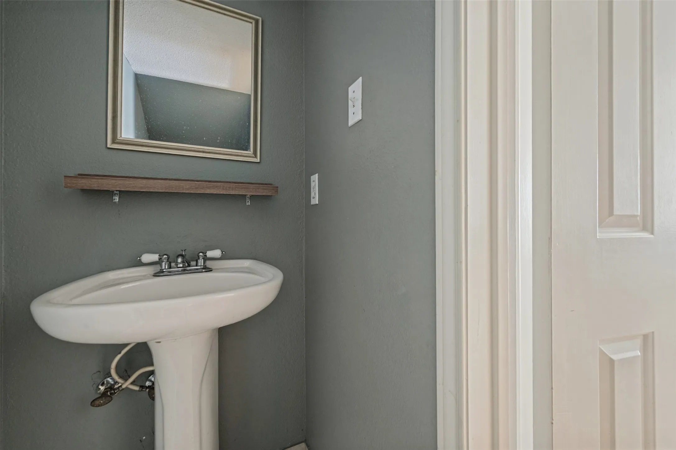 Pedestal sink with chrome faucet, framed mirror, and wood-finish shelving