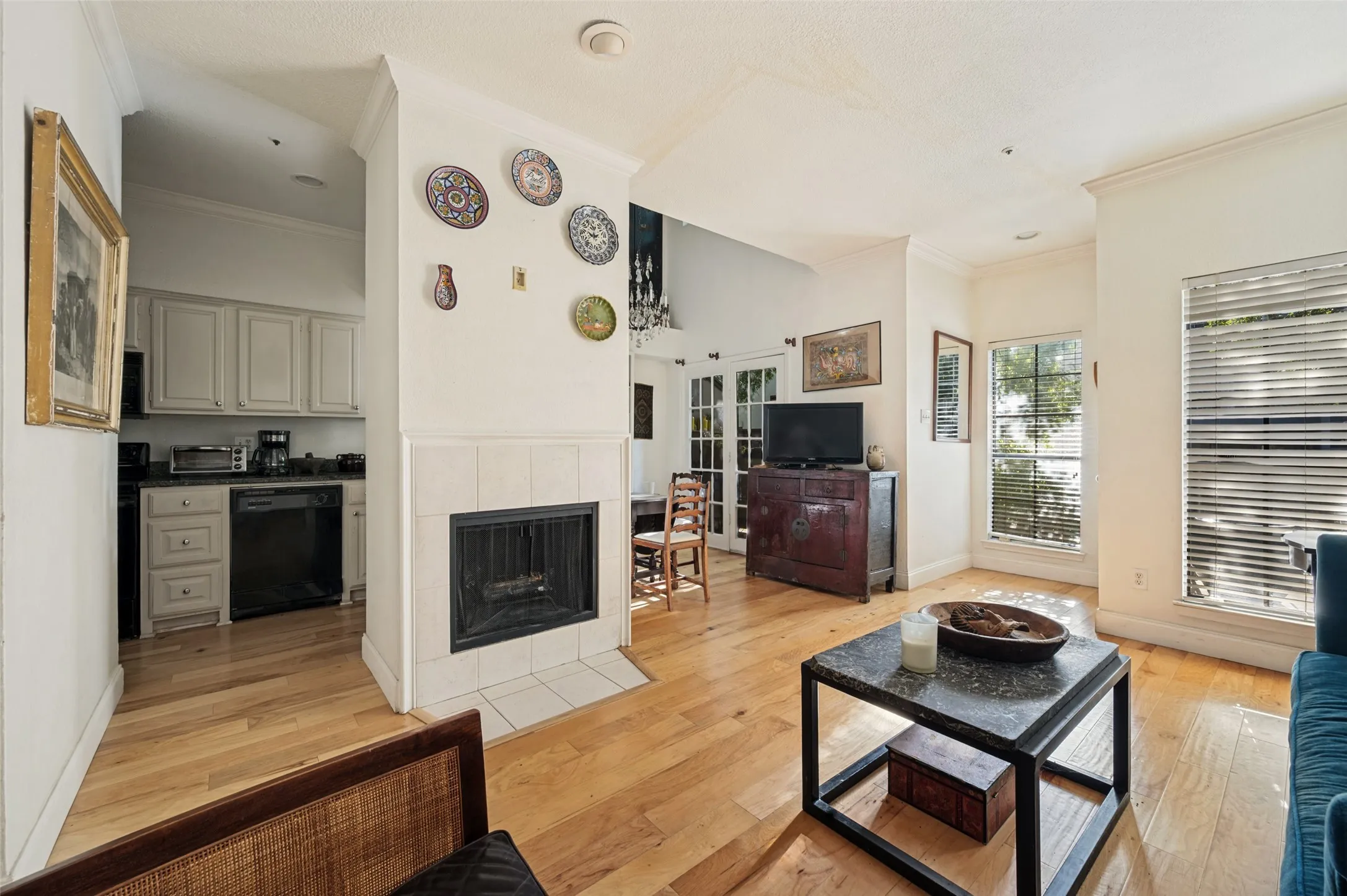 Hardwood flooring, tiled fireplace with hearth, white cabinetry, black appliances, and French doors