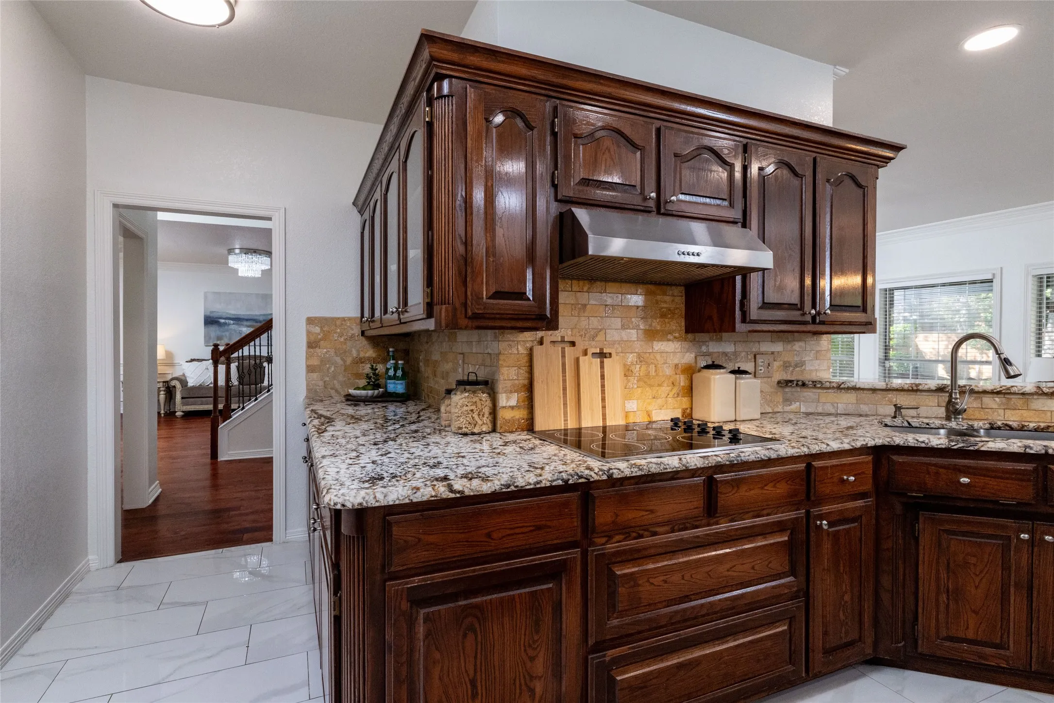 Kitchen featuring rich wood cabinetry, stone countertops, a tile backsplash, stainless steel range hood, and an electric cooktop