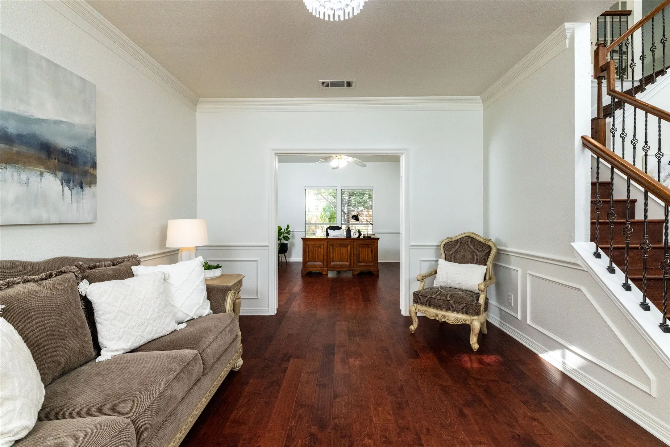 Hardwood flooring, crown molding, wainscoting, open doorway, and a prominent staircase with wrought iron balusters