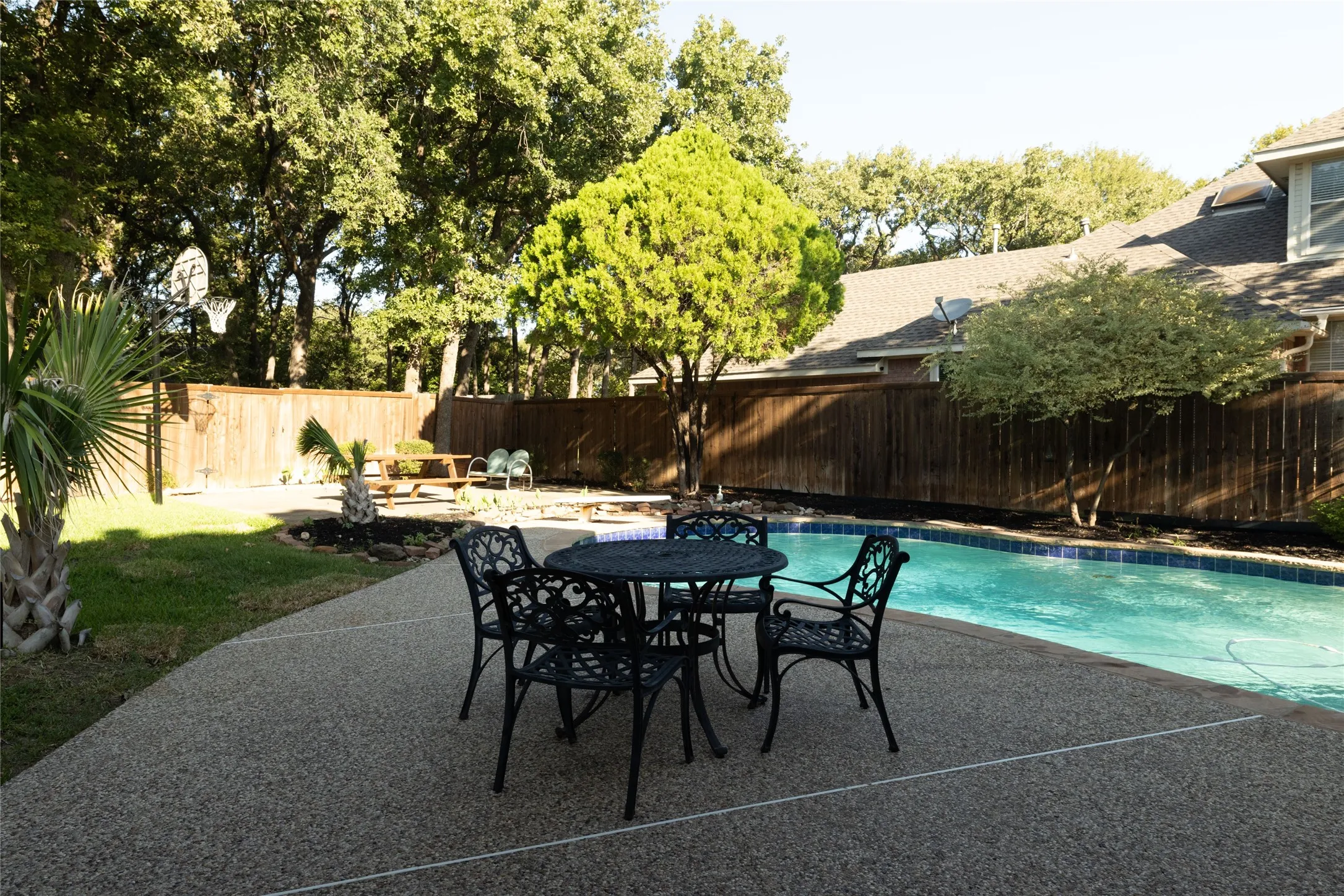 Swimming pool with blue tile surround, concrete patio, and wood privacy fencing