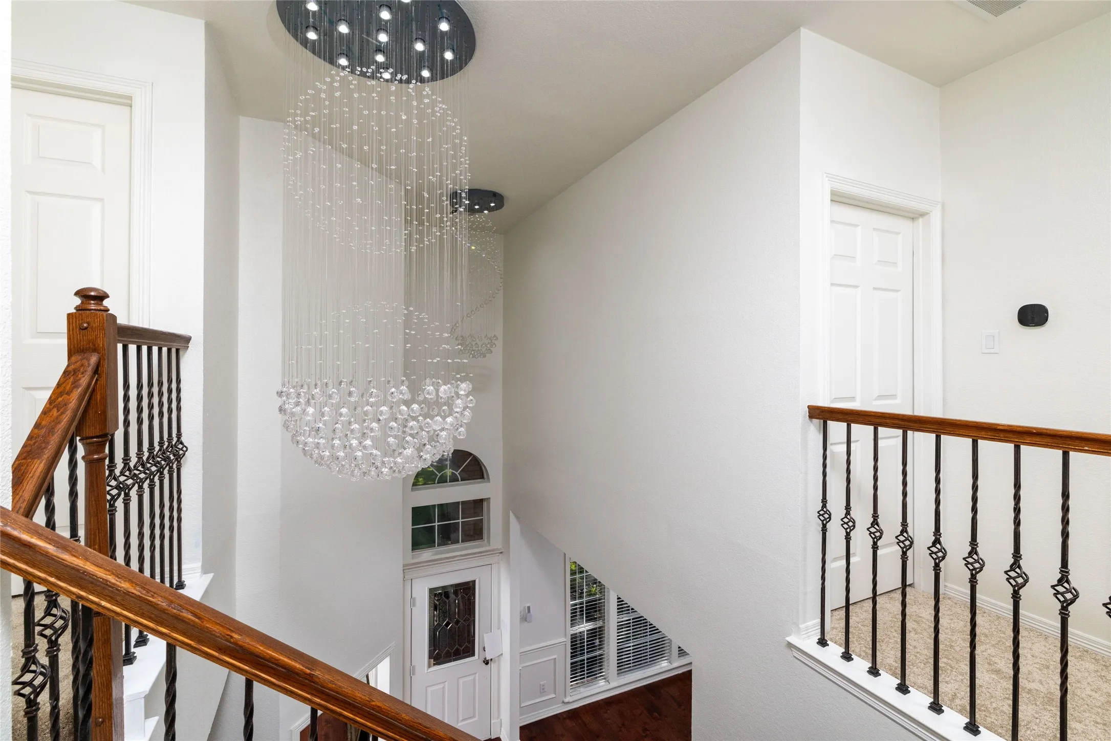 Multi-level foyer featuring dual crystal chandeliers, wood-finish flooring, and a wrought iron and wood banister
