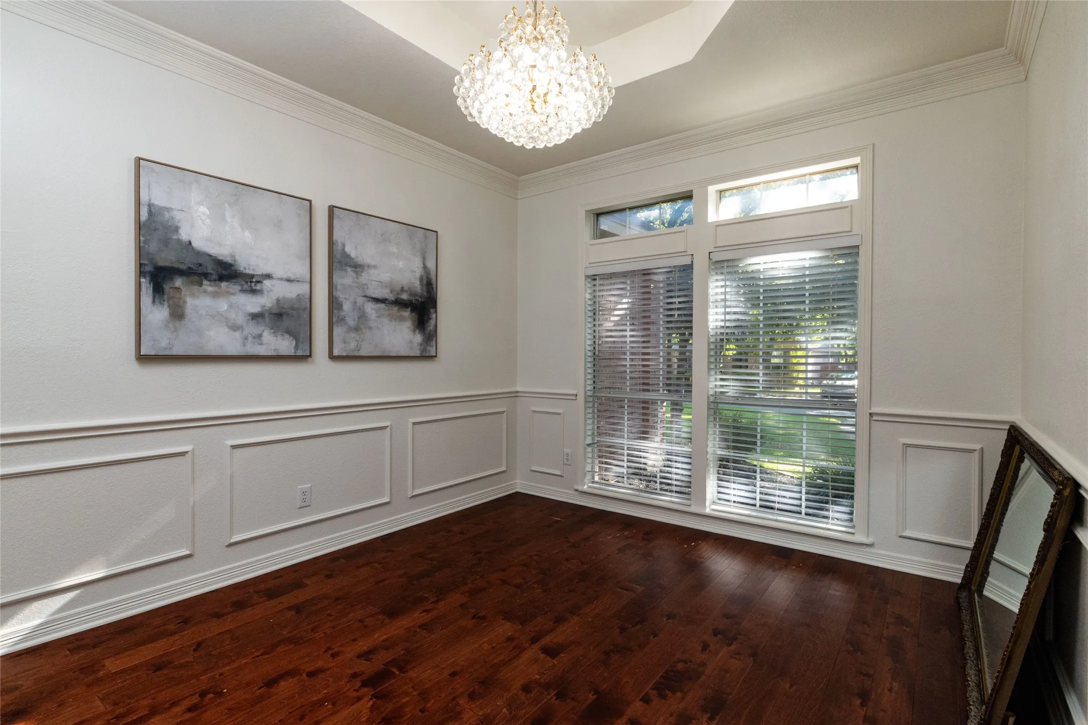 Hardwood flooring, decorative wainscoting, crown molding, tray ceiling, and a crystal chandelier
