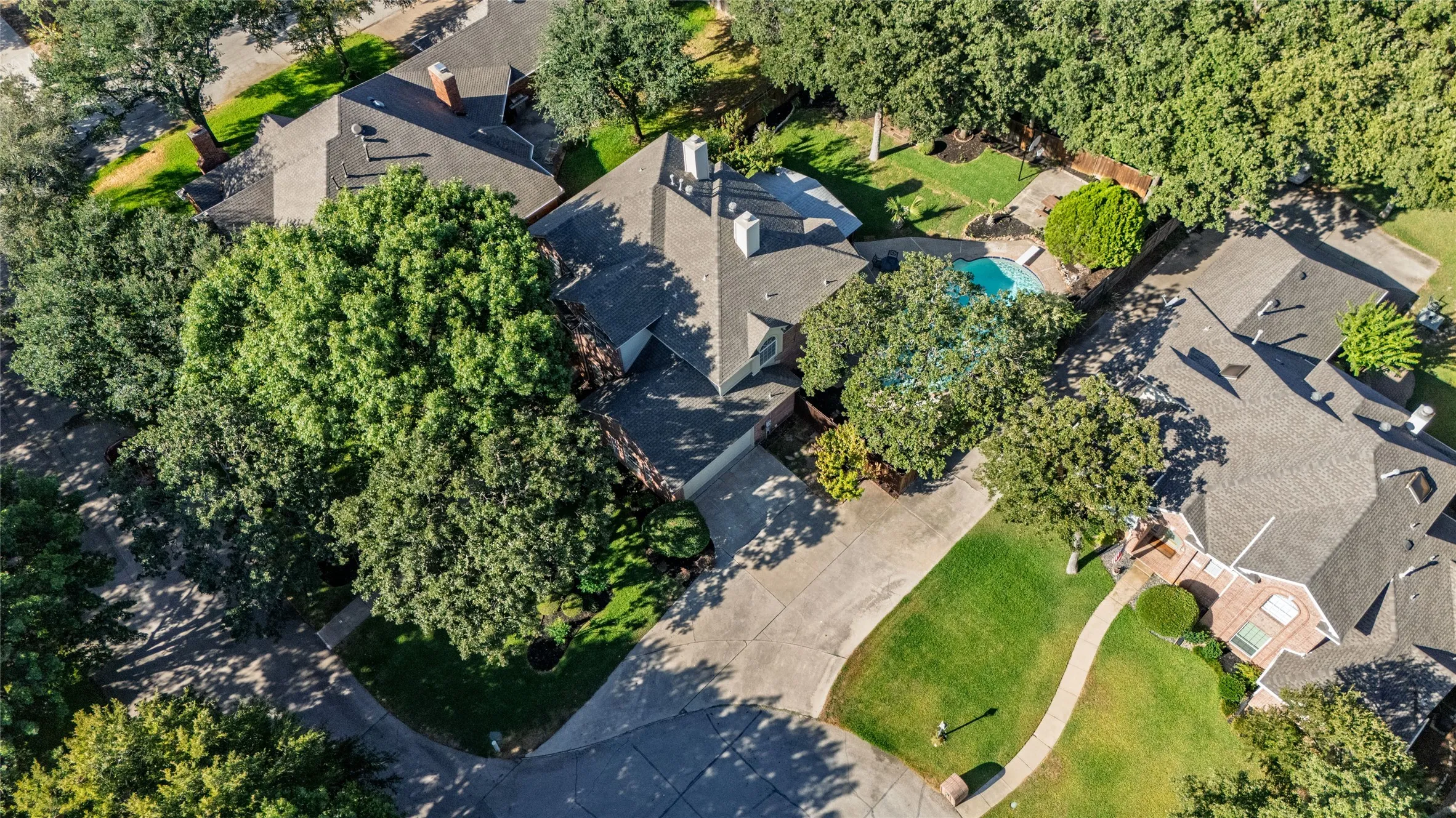 Expansive property featuring a swimming pool, mature trees, green lawns, and a paved driveway