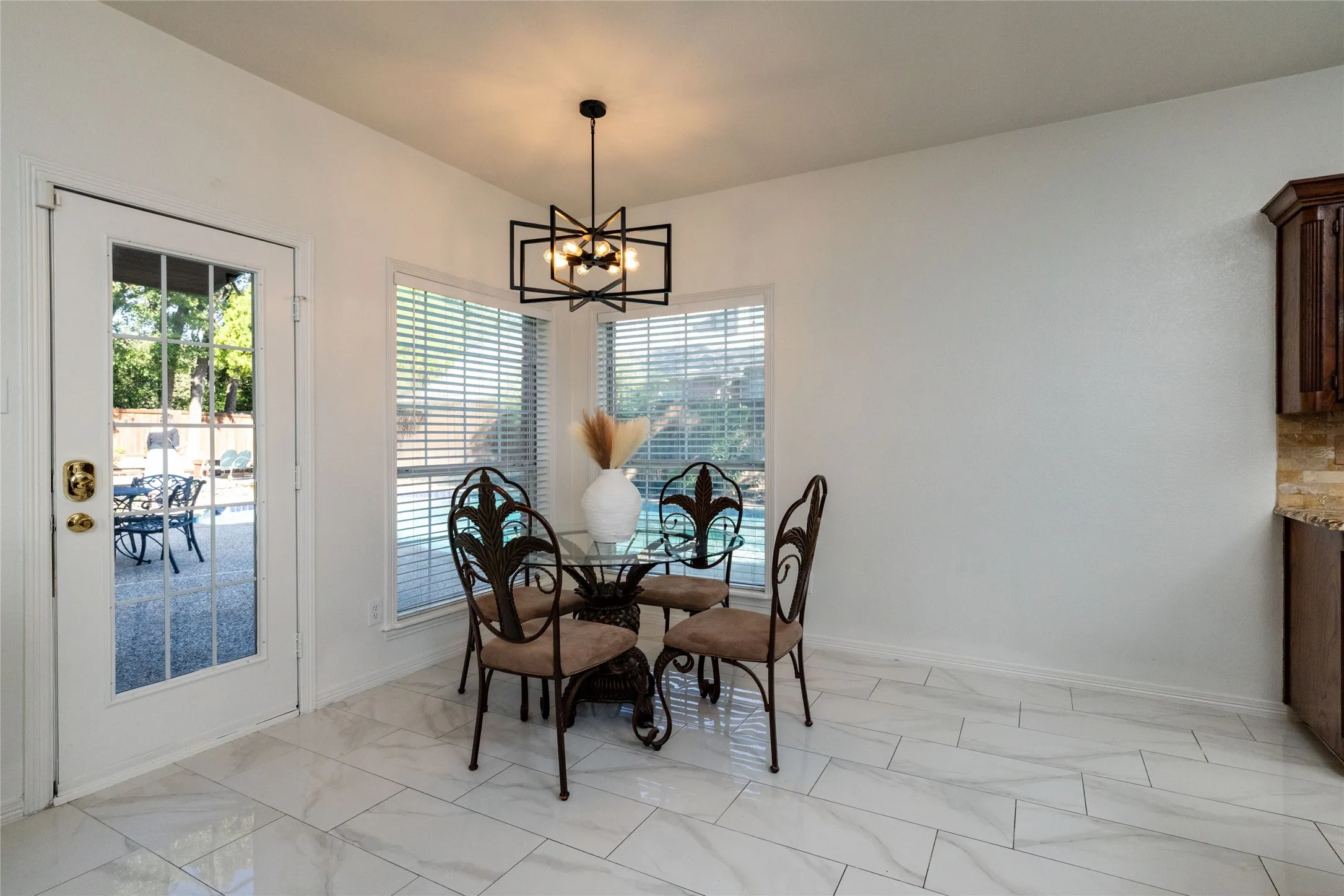 White tile flooring, multiple windows with blinds, a glass-paneled exterior door, and a geometric chandelier