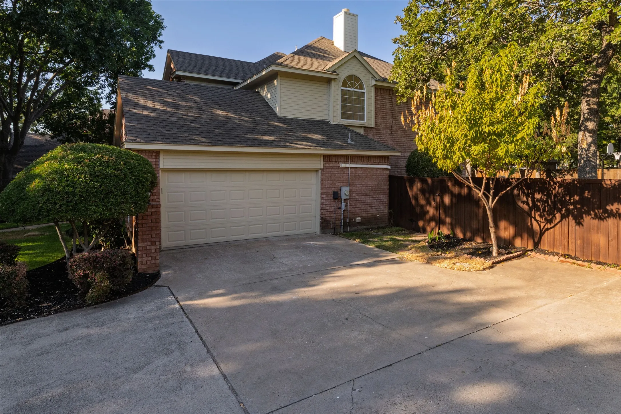 Brick and siding exterior with an arched window, attached two-car garage, and concrete driveway