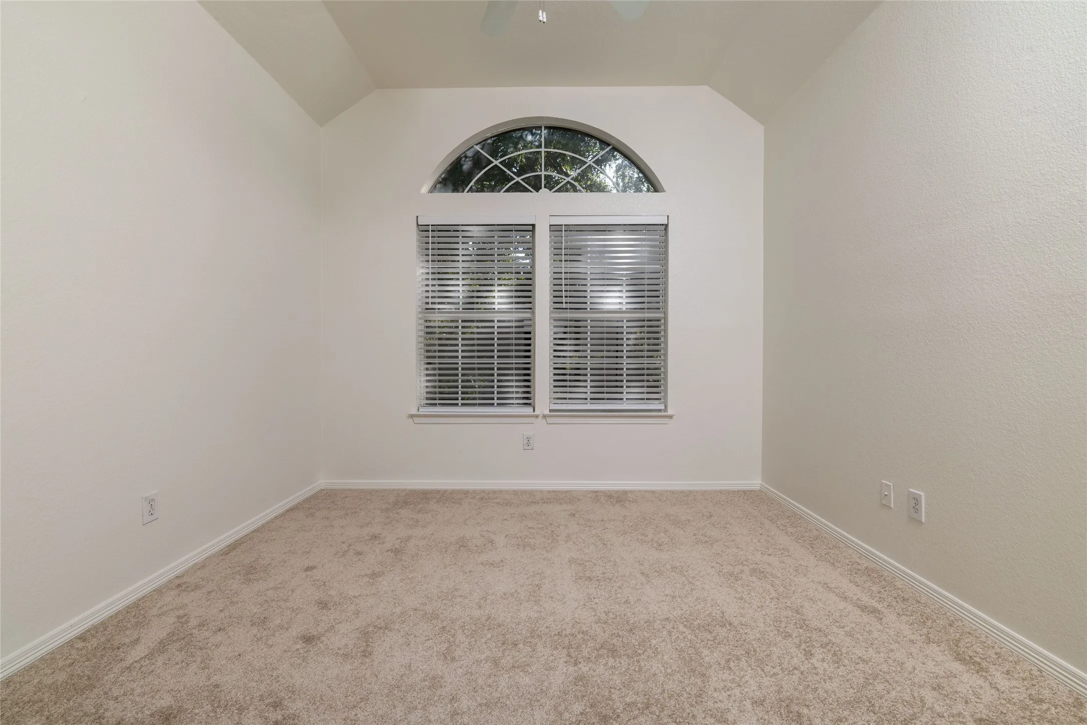 Arched window featuring blinds, vaulted ceiling, and carpet flooring