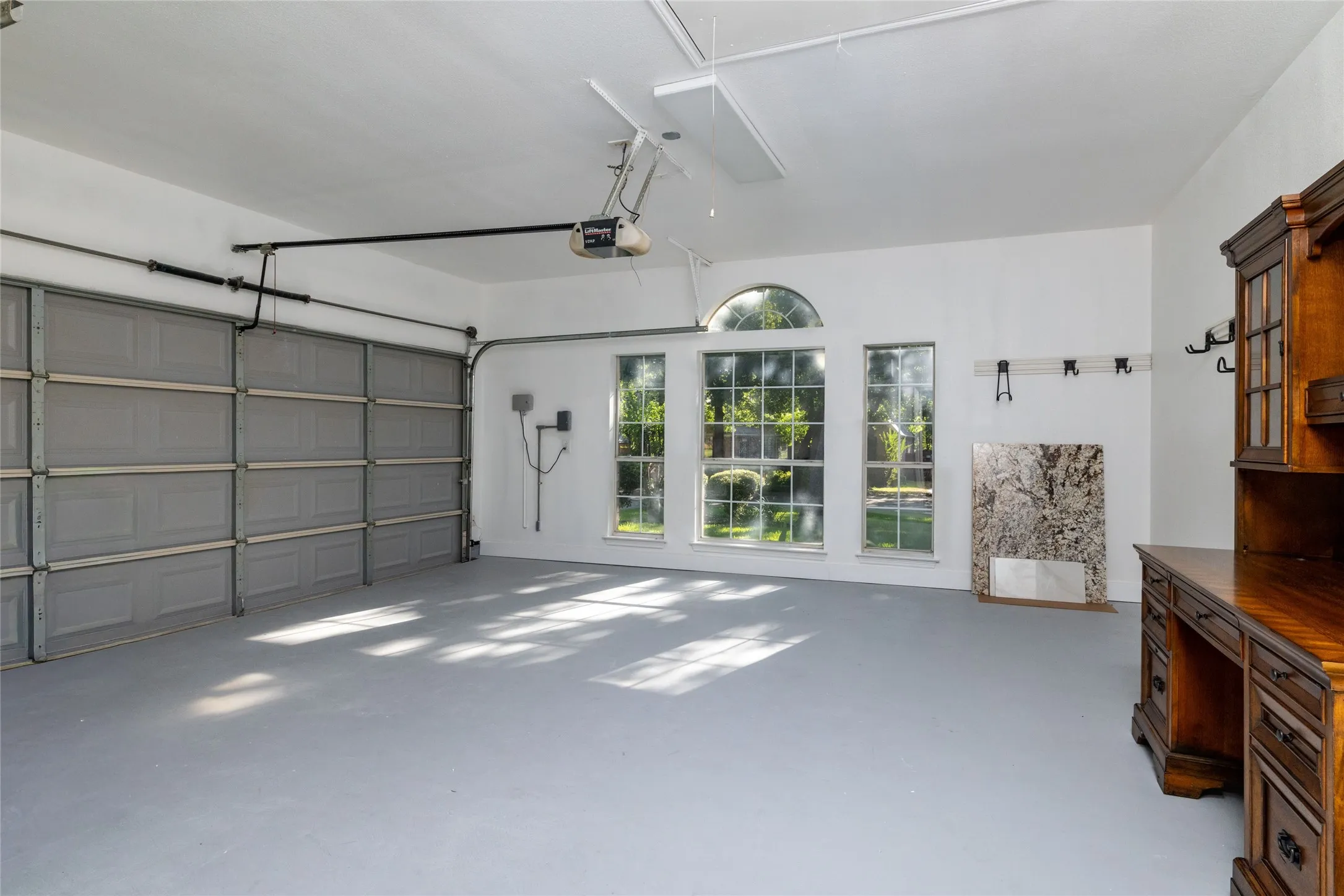 Spacious garage with a light gray painted floor, three large windows including an arched top window, and a built-in garage door with an automatic opener